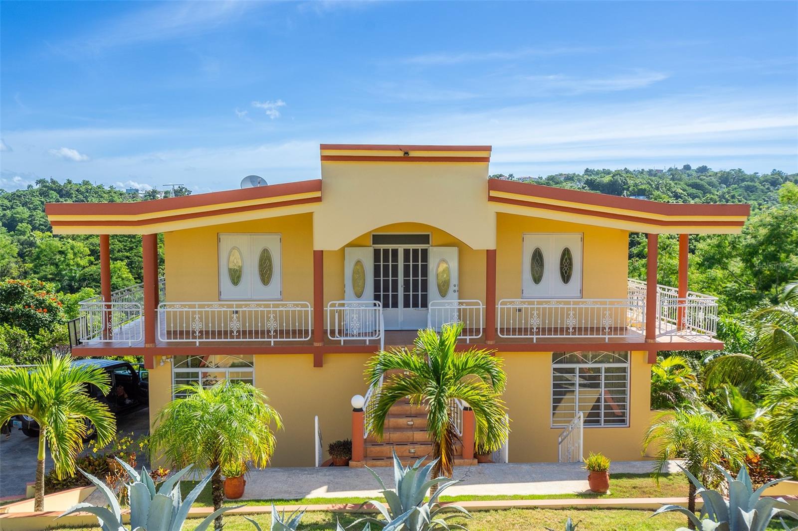 This 3 level, 5 bedroom, 3 bath multi unit house is located in the secluded, scenic Cruces neighborhood in Rincon. The property has just over 2 acres (8,169.8657 sq meters) of land full of hiking and ATV trails and almost every type of fruit tree you can imagine in the Caribbean. In addition to the private jungle full of fruit and palm trees, you will fall in love with the beautifully landscaped lush tropical gardens on the side and in the front of the house. It is a true hillside retreat yet it is only 10 minutes to the iconic beaches and restaurants of Rincon and Aguada. The house has approximately 3,500 SF plus another 500 SF with the covered patio.
The property is already set up for short term rental success and has years of reservations to prove it. The top floor has 2 bedrooms, 1 bath and an open layout for the kitchen, dining and living room. Plus a wrap around balcony with amazing panoramic views of the countryside. The middle floor which is level with the driveway has a very spacious 2 bedroom, 1 bath apartment that includes a kitchen, dining area, living room and a game room with a pool table and darts. There is also a basketball hoop to accommodate a half court game of basketball and sleeps six comfortably. The bottom or ground level has a covered patio overlooking the valley below and a studio apartment with 2 queen beds, a kitchenette and newly renovated bathroom. There is also a very spacious laundry room next door to the studio with plenty of room for storage. Generator and cistern with pump are already installed and included in the purchase. The property will also include all furniture, pool table, appliances and even the ATV to cruise the trails and harvest all the fruit trees.