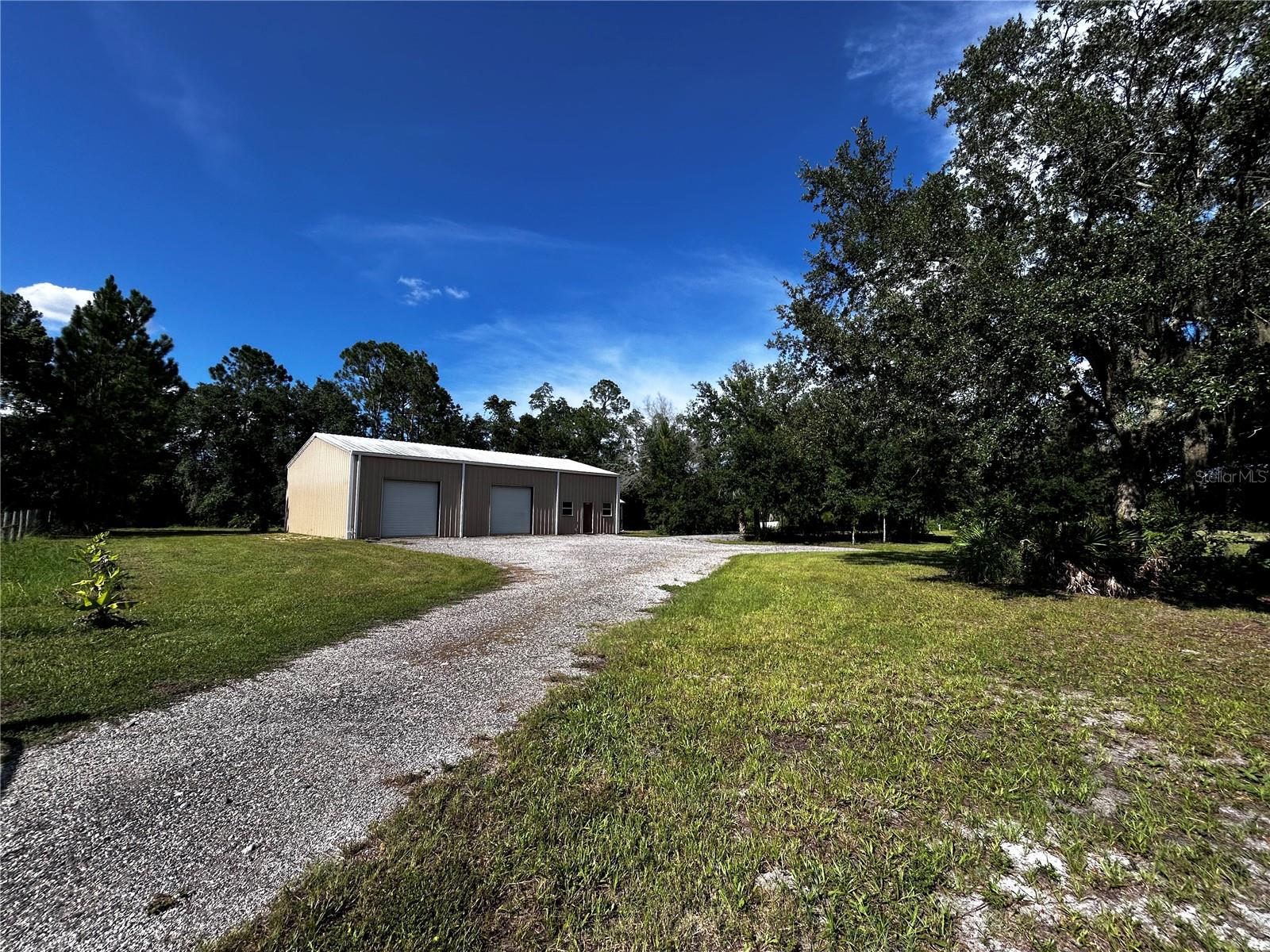 15401 County Road 450 is a slice of natural paradise with nearly infinite future possibilities. Of the 9.46 total acres, 5.86 acres are 'Zone X' dry land, while 3.60 acres are part of a larger wooded wetlands. The wetlands begin at the tree line to the north (back) of the property. This green space offers excellent privacy at the rear of the property and including a tranquil pond. Previous owners had planned to build a home in 2015 before their plans changed. They constructed a 40' x 60' red-iron metal building on the Western end of the property to use for their business, accessible easily by a gate on LeGrande St that enters into a gravel parking area. A 12 x 15 insulated office (drywall interior, plywood facing warehouse) is constructed in the building, plus a 12kBTU minisplit AC installed in 2024 to handle office heating and cooling. The remainder of the building is unfinished with a concrete slab floor. 14' eaves, clear span construction, and three 10' tall roll up doors (3rd door not pictured, faces bathroom building). Near the metal building is a small building with a full bathroom (including shower), plus a utility room with water heater and washer/dryer connections. Power is run underground from the street frontage to the backside of the building, no overhead power lines enter the property! The building has 200amp service, while the drop from the pole to the meter was intentionally oversized in order to adequately service a future 200a house without the need for a new primary utility connection. The well was drilled new in 2015 with water run to the building as well as to various hose spigots scattered around the property. There's a gravel RV pad approximately 12'x60' extending from gravel parking area, 50amp electrical, water, and sewer connection for RV. Plans were submitted to build a 2500sf home, impact fees paid, perk tests performed, but ultimately the house wasn't built and permits cancelled. The impact fees paid will reduce or eliminate additional impact fees for new construction, verify details with county. 15 loads of fill dirt were spread in the field to level and elevate the location they planned to build a house. It has naturally compacted while sitting in place for 8+ years. There is an additional gate directly along the County Road 450 frontage. The initial plan was to build a home on the Eastern side of the parcel, visually separating the home and shop with different entrances and driveways. Greater property depth as well as privacy from the main road on the Eastern side of the property. This land is set up perfectly to build your dream home with plenty of room for dry materials storage during construction in the 2400sf building. Use the building for personal or business use in the future. In addition to water and power already being in place, Lake county allows property owners to live in an RV as long as they have active permits to construct a home on-site. Once the home is completed, long-term living in the RV is no longer allowed. Park your RV for an immediate home-base while building your dream home! Any type of home from manufactured to large custom homes are allowed. Surrounding homes are all on larger parcels, undeveloped land to the West, Ag/Equestrian type surroundings. Convenient to Mt. Dora, Eustis, and The Villages. New builder neighborhoods are stacking homes together at 5-10+ homes per acre, wouldn't it be nice to build a dream home on your own private 9+ acres of peaceful land?