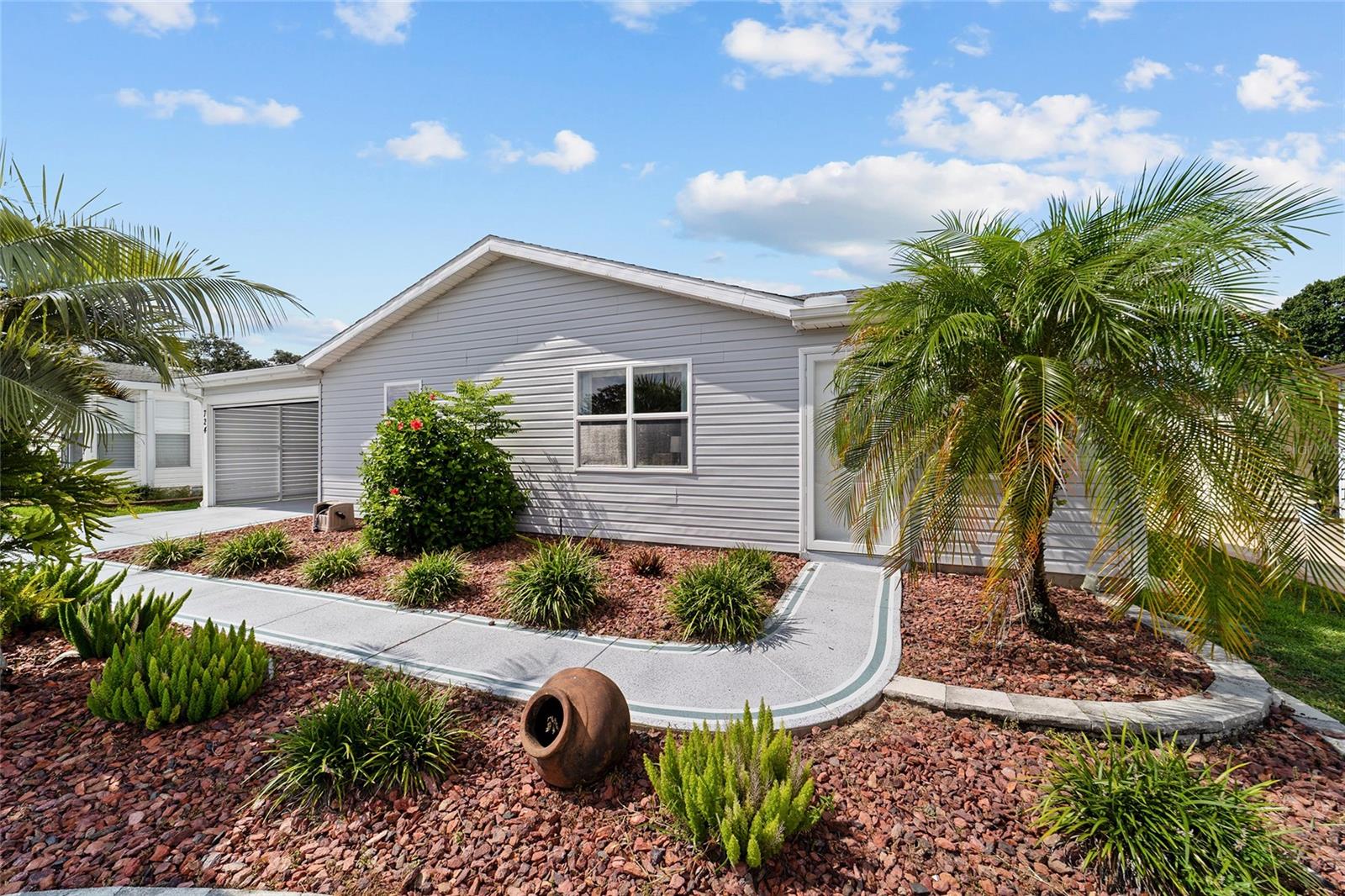 NO BOND and no CDD maintenance tax! This 2-bedroom, 2-bath, wood-framed, site-built slab home in The Villages of Del Mar has it all. It starts with a great location – minutes from the main shopping areas and medical facilities. Minutes by golf cart to either Spanish Springs or Sumter Landing Town squares, as well as three championship golf courses.
As you drive up to the home, you see a nicely manicured lawn, a painted driveway, and hardscape landscaping. As you enter the home, you instantly see quality upgrades and natural light in this updated home. Laminate flooring and tile throughout (NO CARPETING) and high ceilings in the completely OPEN FLOORPLAN. White cabinets, GRANITE COUNTERTOPS, and STAINLESS STEEL APPLIANCES. Large primary bedroom with a walk-in closet and an en-suite bathroom with dual sinks and solid surface countertops. A beautiful sunroom off the living room can be an office, hobby room, gym, or just additional living space.
Now let’s discuss the functional aspects of the home: This home has a carport with a remote-controlled ROLL-UP SCREEN DOOR. Off the carport, there is an oversized utility/laundry/storage room AND a golf cart garage with its own entrance.
Whole-house water filter included. BRAND NEW VINYL SIDING and upgraded windows. HVAC is 6 years old, and the roof is 2014.