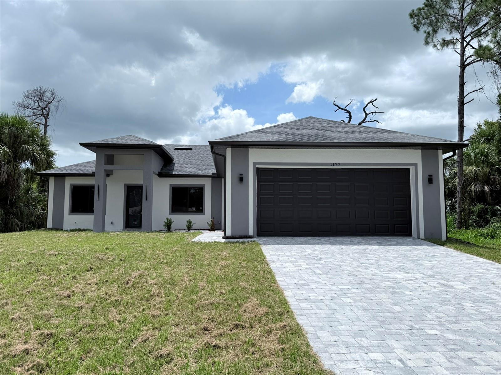 Introducing a newly constructed four-bedroom, three-bath residence in the heart of North Port. Spanning 2,153 square feet of living space and totaling 3,099 square feet, this home combines modern architecture with function and refined detail. The open-concept floor plan seamlessly integrates living and dining areas, creating an inviting space for daily living and entertaining. A gourmet kitchen anchors the interior, featuring state-of-the-art stainless steel appliances and luxury finishes. High-quality vinyl flooring runs throughout, complementing soaring 10-, 12- and 13-foot ceilings that enhance the home's scale and light. The primary suite is a private retreat with a spa-style bath including a soaking tub, walk-in shower, double vanity and an oversized walk-in closet. Additional features include a laundry room with sink and pre-designed layout for future home enhancements. Thoughtful exterior design includes modern elevation details, sliding windows, a metal and glass front door, soffit lighting in the rear area and strategically placed gutters. The home sits on a site ready for a pool and has summer kitchen connections ready. Built in 2025 with an emphasis on craftsmanship and contemporary design, this property presents a rare opportunity to own a new construction home in an established area of North Port.