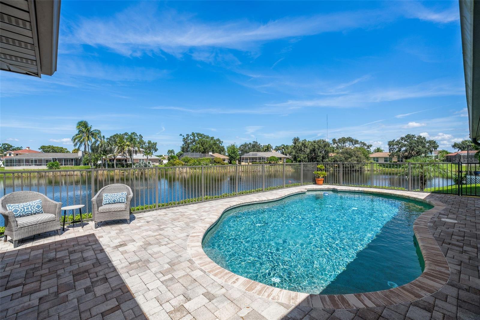 Discover the elegance of Riviera Bay, an established waterfront community, with this meticulously maintained lakefront pool home—a true rarity. Important to note: this home has never flooded! As you approach, you'll be impressed by the mature landscape, paver driveway, and inviting entry that set the tone for this unique property. Step inside to a welcoming foyer adorned with travertine tile floors, leading you to rooms that boast beautiful water views. Enjoy the warmth of the sunroom's wood-burning fireplace or entertain in the beautiful dining and living rooms. For dining al fresco, the tranquil poolside setting by the quiet lake offers the perfect ambiance, day or night.
Inside, the kitchen stands out with white Kraftmaid cabinets, some featuring glass fronts for displaying your cherished items. It is complemented by granite countertops, stainless steel appliances, and a spacious breakfast bar. Adjacent, the large family room, enhanced by custom cabinetry, provides a cozy space for gatherings or TV time. Retreat to the primary bedroom, a serene space with an en suite bath, walk-in shower, and custom vanity. The generously sized second bedroom also features an en suite full bath, while the versatile third bedroom can serve as a home office, workout space, nursery, or playroom, conveniently located near the third full bath with a jacuzzi tub.
This home showcases attention to detail, with features like a sizable laundry room, plantation shutters, crown molding, recessed lighting, custom cabinetry, aluminum pool deck fencing, exterior lighting, and an irrigation system using reclaimed water. The property's prime location offers proximity to Tampa, Clearwater, downtown St. Petersburg, shopping, and dining, just minutes away. Schedule your private showing today!