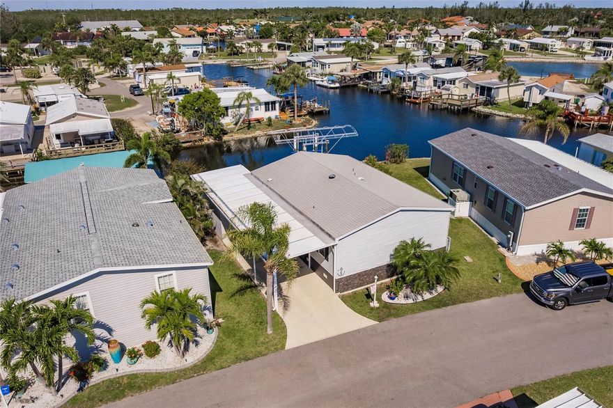 Welcome to your piece of paradise! This spacious 1,080 sq. ft. waterfront home, built in 2005, is located in the highly sought-after, 55+ resident-owned, gated community of Windmill Village in beautiful Punta Gorda. Offering 2 bedrooms, 2 bathrooms, and a wealth of desirable features, this home sits on a generously sized lot with 61 feet of waterfront along the serene Tarpon Canal. Boating enthusiasts will love the 6,000-pound covered boat lift and dock, providing direct access to the water for effortless enjoyment of Florida’s boating lifestyle. Canals are Windmill Village waterways. Step inside to discover an inviting open floor plan featuring a bright living room, dedicated dining area, and a chef-inspired kitchen. The kitchen showcases stainless steel appliances, granite countertops, ample cabinetry, and a large center island with seating—ideal for casual meals or entertaining. The adjoining dining area includes a granite-topped dry bar with a wine rack, beverage refrigerator, and extra storage. The living area offers sliding glass doors that open to the back deck, where you can relax and take in stunning waterfront views. Throughout the home, you’ll find luxury vinyl flooring, carpeted bedrooms, and elegant crown molding. Major upgrades include a new roof (2019), A/C (2019), and water heater (2022)—offering peace of mind for years to come. The primary suite features a walk-in closet and a beautifully updated en-suite bathroom with a spa-like walk-in shower, complete with multiple showerheads, frameless glass doors, and classic subway tile walls. The second bedroom is generously sized and conveniently located next to a full guest bathroom. Laundry located in hallway closets has updated washer and dryer. Need extra storage? You’re covered. The home includes a spacious attached storage garage with double roll-up doors—perfect for tools, water toys, or workshop space, offering both convenience and functionality. Windmill Village provides a vibrant, active lifestyle with amenities that include two private marinas, a boat ramp, trailer storage, shuffleboard, bocce ball, horseshoe pits, indoor pickleball courts, billiards, and a large community center filled with clubs and activities. The newly built Pavilion by the heated pool is a perfect gathering spot for residents and events. Please note: the purchase price does not include the $20,285 Buy-In Share and Bond, which is refundable upon resale.
