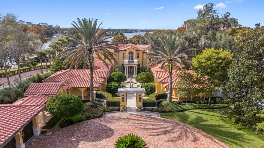 Elegant Mediterranean estate, masterfully crafted by Akers Custom Homes and set within the heart of the Vias. Privately tucked behind a gated drive, the approach unfolds to a grand circular motor court framed by lush, manicured grounds spanning over two acres with impressive sunset views across Lake Maitland. Every element of the estate is thoughtfully connected by covered walkways, including five garages (three-car and two-car) and two motor courts, a detached office or seventh bedroom suite, and a lakeside pool cabana, creating a seamless blend of function, elegance and architectural harmony in this one-owner Lake Maitland residence. A dramatic arrival sets the tone as a flowing water feature guides guests along the walkway to the front entry. Inside, the grand foyer opens to a breathtaking gathering room, anchored by soaring two-story windows that frame panoramic lake views, the expansive terrace and terraced outdoor space. A dedicated space for a grand piano enhances the home’s capacity for elegant entertainment and memorable gatherings. The spacious kitchen overlooks the family room and is positioned alongside a dedicated bar, breakfast room and dining room. The family room, warmed by a gas fireplace, is filled with natural light and opens through a wall of French doors to the open terrace, blurring the line between indoor and outdoor living. The first-floor primary suite is a serene retreat with French doors to a covered outdoor space, a fireside sitting area wrapped in custom bookshelves, and a spa-inspired bath featuring a large glass shower, soaking tub, expansive walk-in closet, and a versatile flex room ideal for yoga, massage or expanded wardrobe space. A full guest suite with en-suite bath and walk-in closet is also on the main level. Upstairs, a grand mezzanine overlooks the gathering room, offering a dramatic extension of the living areas. French doors open to a front balcony, while the west wing features two bedrooms with a shared private living room and full bath. The east wing hosts two additional bedroom suites, each with walk-in closets and en-suite baths, one enhanced by a private sitting area and access to a spacious rear balcony. Off the kitchen, a wrought-iron gate leads to the basement level, where a refrigerated wine cellar, theater room, and generous storage space await. Outdoors, the stunning terrace showcases a heated spa, sparkling lakeside pool, expansive gas fire pit and an extraordinary 700-square-foot pool cabana that offers a wraparound screened porch with summer kitchen, a full bar, gaming area and full bath, ideal for lakeside entertaining. Elevated above the water for commanding views and shielded from the main road for complete privacy, this remarkable estate is a masterpiece, designed for multi-generational living and destined to create lasting memories for generations to come.