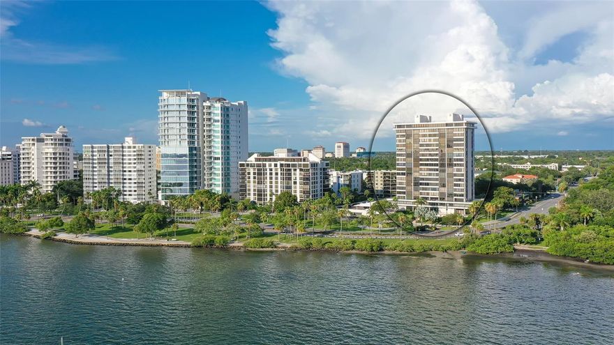 Perched on the 7th floor, this exceptional residence delivers truly breathtaking panoramic vistas. Set within a landmark building designed for refined downtown living at the quiet end of Palm Avenue, the residence enjoys a premier location along the Bayfront with sweeping views of Sarasota’s most sought-after scenery. From the sparkling bay and sailboats lining Bayfront Park to the John Ringling Bridge, Golden Gate Point, Bird Key, Lido and Siesta Keys, the Gulf waters, and Selby Gardens—every direction offers a postcard-worthy outlook.
A semi-private elevator entry welcomes you into a beautifully furnished condo with uninterrupted water views unfolding as you step inside. The expansive living spaces feature an open, flowing layout anchored by a dramatic 30-foot expanse of west-facing glass and wood flooring. Living, dining, kitchen, and sitting areas are all designed to showcase the ever-changing scenery, from glowing sunrises to unforgettable sunsets. Enjoy floor to ceiling bookshelves in the great room.  The kitchen has custom granite countertops, stainless appliances, insta-hot water, white glass-front display cabinets, and extraordinary storage. Views from the primary suite span from the Bayfront to the heart of the city. A generous size bath and walk-in closet are pluses. The guest quarters and bath provide the perfect retreat for your guests. 
Embassy House is a secure and meticulously maintained example of modern architectural design. Its recently refreshed lobby and amenities reflect a sophisticated mid-century modern aesthetic, complete with bespoke furnishings and carefully selected artwork.
Residents enjoy an impressive collection of amenities, including a bay-view fitness center, conference space with kitchenette, a renovated heated pool, guest parking, electric vehicle charging, car wash station, grilling area, and outdoor dining spaces.
Whether your ideal day involves quiet mornings with coffee overlooking the water, hosting evening gatherings with cocktails, or strolling to nearby cafés, restaurants, shops, galleries, the bayfront, Selby Gardens, or the Saturday Farmers Market, this location supports every lifestyle. This is where elevated coastal living truly begins.