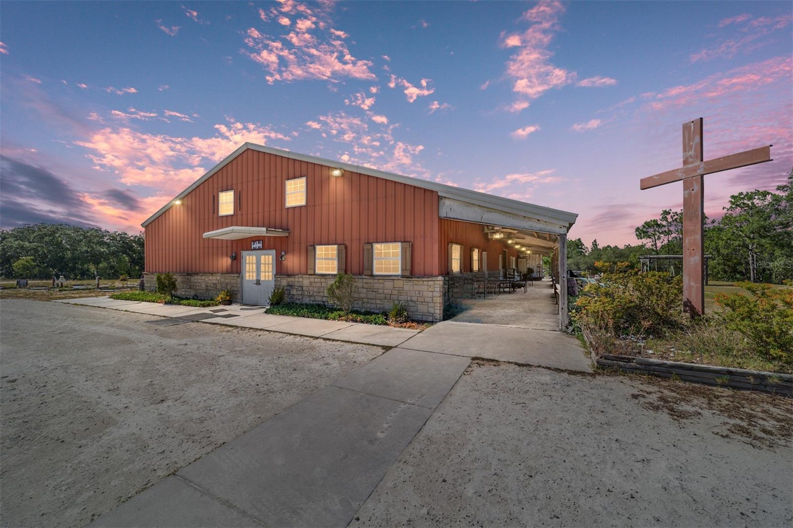 IMAGINE THE POSSIBILITIES! Set on 20 expansive acres, this one-of-a-kind property offers endless potential for your vision! Whether you dream of a unique residential conversion, custom farm or bringing your congregation to the country, this sprawling 5,000+ sq. ft., two-story metal building is ready to accommodate your needs. INSIDE THE MAIN BUILDING - DOWNSTAIRS features a massive 40’ x 50’ open space with soaring 18’ ceilings, perfect for large gatherings, events, or creative use. A full commercial-style kitchen includes a convenient pass-through for both indoor and outdoor service. With separate men’s and women’s restrooms, additional wheelchair-accessible facilities, six flexible classrooms (each ~200 sq. ft.), and a 400 sq. ft. storage room, this space is primed for a variety of uses. Six commercial A/C units ensure year-round comfort. UPSTAIRS, you’ll find two office spaces, a sound booth overlooking the main open area, lots of storage spaces and a laundry room with a ½ bath—ideal for administrative or residential use. OUTSIDE FEATURES & ADDITIONAL STRUCTURES - Enjoy the full-length covered porch, a 2 acre parking area, and remnants of a putt-putt course and shuffleboard court, offering unique recreational possibilities. Two small log buildings, ready for restoration, add to the character of the property. Also included is a 1,150 sq. ft. manufactured home with 3 bedrooms and 2 baths, perfect for on-site living or rental income. With limitless potential, this versatile property is ready for its next chapter. Don’t miss this rare opportunity—schedule your showing today!