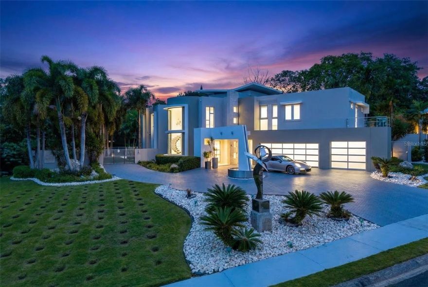 Casa Aurelia is a custom-built architectural estate located on the west side of Puerto Rico, offering a rare combination of scale, design, and privacy. Designed by architect Roberto Melendez and featuring interiors by Beatriz Nieves, this residence spans approximately 8,033 square feet across two combined lots totaling over 5,000 square meters.

The home features 6 bedrooms and 5.5 bathrooms, all finished in marble, along with curated design elements including curved glass details, a floating quartz staircase, textured wall finishes, and solid wood doors throughout. The open-concept layout is distributed across two levels, creating spacious living areas with seamless indoor-outdoor flow.

Interior highlights include a private home theater, a large wine cellar, and smart home features designed for comfort and convenience. The kitchen is equipped with premium Monogram appliances, quartz countertops, and an ice maker, while multiple living and dining areas provide flexibility for both everyday use and entertaining.

The outdoor space offers a resort-style experience with a saline pool featuring a luminous finish, integrated quartz seating, a jacuzzi, and a fully equipped outdoor kitchen. The landscaped grounds include a custom stainless steel sculpture, an artist-designed front fountain, and an integrated sound system throughout the pool and garden areas.

Additional features include two power generators (20k gas and 40k diesel) with transfer switch, two water cisterns, a private well, irrigation system, security alarm, electric gate, and dog enclosures. The property is located within a controlled-access community of approximately 60 residences, providing privacy and security.

Casa Aurelia presents a unique opportunity to own a fully custom architectural home in Puerto Rico, combining modern design, functional living, and resort-style amenities in one of the island’s most private residential settings.