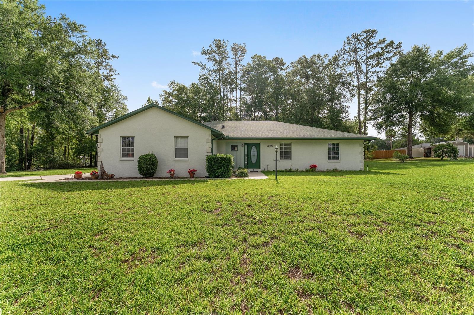Looking for your private oasis on .62 acres and close to everything? This is it! This meticulously maintained 3-bedroom + office, 2-bathroom home sits on a rare double lot with no neighbors on one side—thanks to a neighboring retention pond that ensures privacy and protects against future development. The inviting side porch features a charming swing, while the enclosed front porch has been thoughtfully converted into a bright, functional office space. Inside, you’ll find vaulted ceilings, newer flooring throughout the main living areas, and a spacious, well-designed layout. The primary suite includes double vanities and a generously sized walk-in closet. A separate indoor laundry room with a utility sink adds everyday convenience. Major upgrades include a newer A/C and water heater, a water softener system, and a roof that’s just one year old. Outside, the property offers both an attached 2 car garage and a detached two-car garage with electric, an additional powered shed, and a cleared backyard with no overhanging trees—providing peace of mind during storm season. Additional features include gutters, a sprinkler system, well and septic, and plenty of room to spread out. This home blends comfort, privacy, and long-term peace of mind. Did I mention no HOA? Located 15 minutes from The Villages and 15 Minutes from Ocala for the best of both worlds!