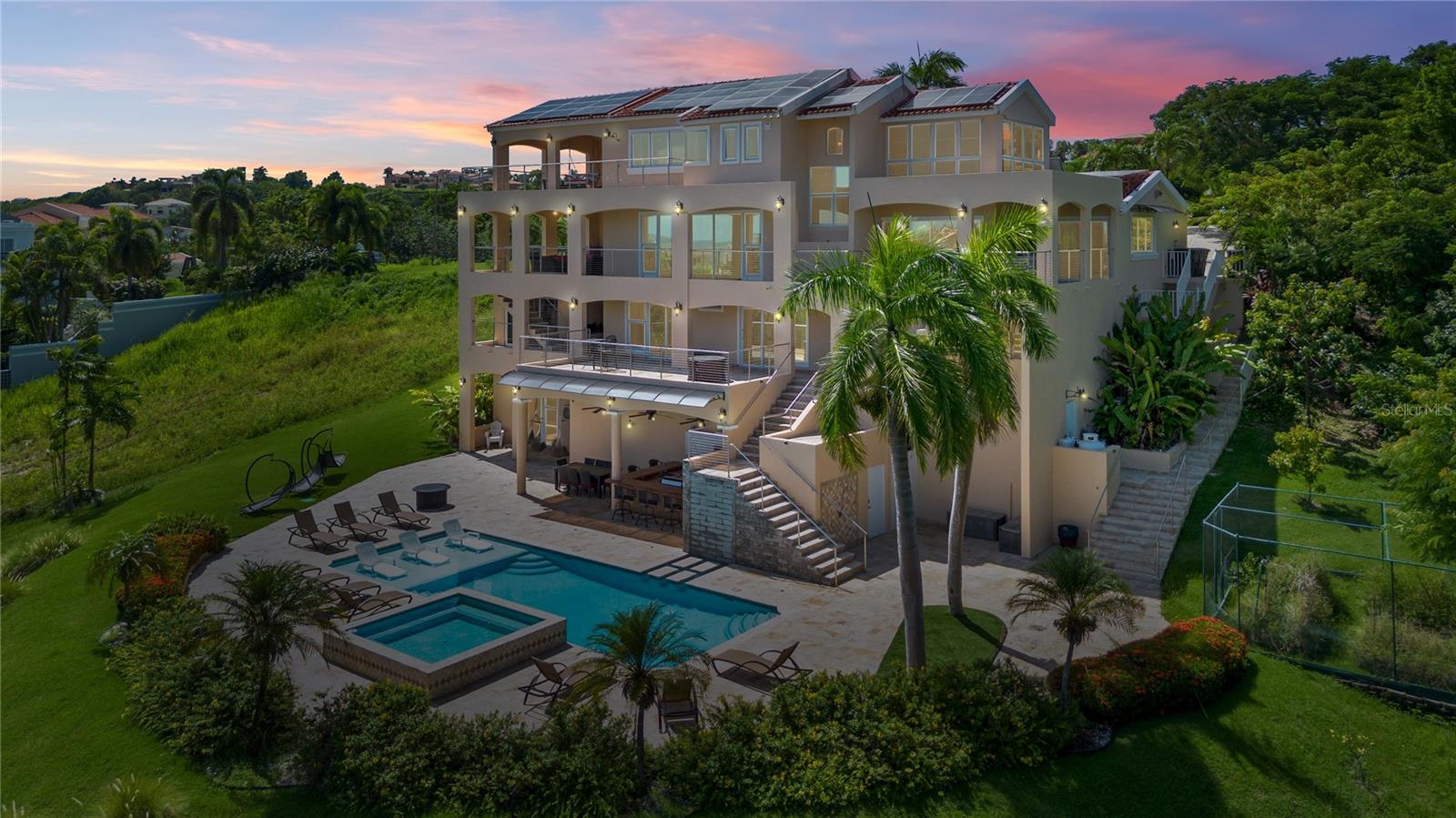 Discover unparalleled luxury and style in this magnificent property nestled in the rolling hills of the coveted Palmas del Mar resort. This exquisite 4-level estate spans over half an acre, surrounded by lush fruit trees, offering serenity, privacy, and breathtaking panoramic views of the ocean and marina. Built to perfection in 2018, its Contemporary Mediterranean design unfolds across an expansive 14,000 square feet, including 7,000 square feet of interior elegance and a vast outdoor oasis. With 8 luxurious bedrooms and 8.5 bathrooms, every corner exudes opulence.
The grand foyer showcases exquisite craftsmanship, leading to a splendid guest suite, an elegant powder room, and a state-of-the-art kitchen. Adjacent, the dining room and grand living area invite guests to unwind, seamlessly extending to a lavish covered terrace with an outdoor kitchen, epitomizing high-end entertainment. The second level houses most of the bedrooms, bathrooms, a media retreat, ample storage, a laundry area, and a 3-car garage. The primary sanctuary, located on the fourth level, features a private office, an additional laundry facility, and an exclusive covered terrace, ensuring unmatched tranquility.
The lower level is an entertainer's dream, boasting a luxurious outdoor area with a sparkling pool featuring a soothing water element, a heated Jacuzzi, a full outdoor kitchen, and a bar. Embracing sustainability, the property is powered by 50 solar panels with batteries, a robust 22 KW generator, and an 18,000-gallon cistern.
Within the gated community of Palmas del Mar, immerse yourself in world-class amenities such as championship golf courses, tennis courts, an equestrian center, The Palmas Academy, and a variety of dining and shopping options. Just 30 miles from Luis Muñoz MarÃn International Airport in San Juan, this residence represents the pinnacle of resort living, offering a harmonious blend of serenity, security, and convenience. Welcome to the height of luxury in Palmas. Annual HOA fee: $1,300.