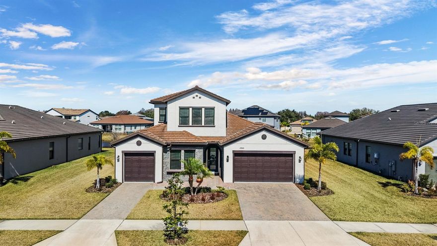 Welcome to refined elegance in the gated community of Tarramor, where architectural detail, thoughtful design, and tranquil pond views come together seamlessly. From the moment you arrive, the home’s stately curb appeal makes a lasting impression, featuring a split three-car garage, paver driveway, and striking brick accents that frame a dramatic arched entry. The covered front corridor creates a true sense of arrival before stepping through the custom glass front door. Inside, soaring ceilings and expansive sightlines immediately draw your eye through the home to the water beyond. Wood-look ceramic tile flows throughout the main living areas, blending warmth with durability. The open design offers both sophistication and comfort, ideal for entertaining or everyday living. The gourmet kitchen serves as the centerpiece of the home, thoughtfully designed for both everyday function and elevated entertaining. An oversized quartz island anchors the space, complemented by wall to wall full-overlay cabinetry with crown molding, satin nickel hardware, under-cabinet lighting,and GE stainless steel appliances. A built-in oven and microwave, gas cooktop, and generous pantry enhance both form and practicality. Designer pendant lighting and abundant natural light from the dinette area create a bright, welcoming atmosphere while you enjoy peaceful pond views. The centrally located family room connects seamlessly to the dining space and kitchen, offering an expansive setting for gatherings while maintaining an intimate feel. The primary suite is privately positioned and designed as a retreat, featuring tray ceilings, a statement ceiling fan, and serene views. The spa-inspired bath includes split quartz vanities, a soaking tub, a large walk-in shower with bench seating and dual shower heads including a rain feature, a private water closet, and a custom walk-in closet system. A junior suite provides privacy for guests or multi-generational living, while two additional bedrooms share a beautifully appointed bath with custom shower and tile finishes. The split layout ensures comfort and separation for everyone. Upstairs, a remarkable 21 x 22 bonus room with its own half bath and walk-in storage offers flexibility rarely found in primarily single-level homes. Whether envisioned as a media lounge, executive office, fitness studio, game room, or fifth bedroom, this space adapts effortlessly to your lifestyle. Set on a generous quarter-acre homesite, the backyard provides ample green space for pets, play, or future outdoor enhancements. The covered lanai creates an inviting setting for sunset evenings overlooking the water. Additional features include epoxy-coated garage floors, Wi-Fi smart garage openers, storm shutters, whole-house water softener, custom guest bath tile work, and refined finishes throughout. Beyond the home itself, Tarramor residents enjoy resort-style amenities and direct access to the Suncoast Trail, one of Florida’s longest paved biking and walking trails, perfect for an active outdoor lifestyle. Zoned for top-rated public schools and ideally situated just minutes from the Suncoast Parkway, this location provides convenient access to Tampa’s premier shopping, dining, golf courses, hospitals, Riverwalk, and the world-renowned Gulf beaches. International Plaza and Tampa International Airport are less than 30 minutes away. This is more than a home. It is a lifestyle defined by design, location, and refined living.