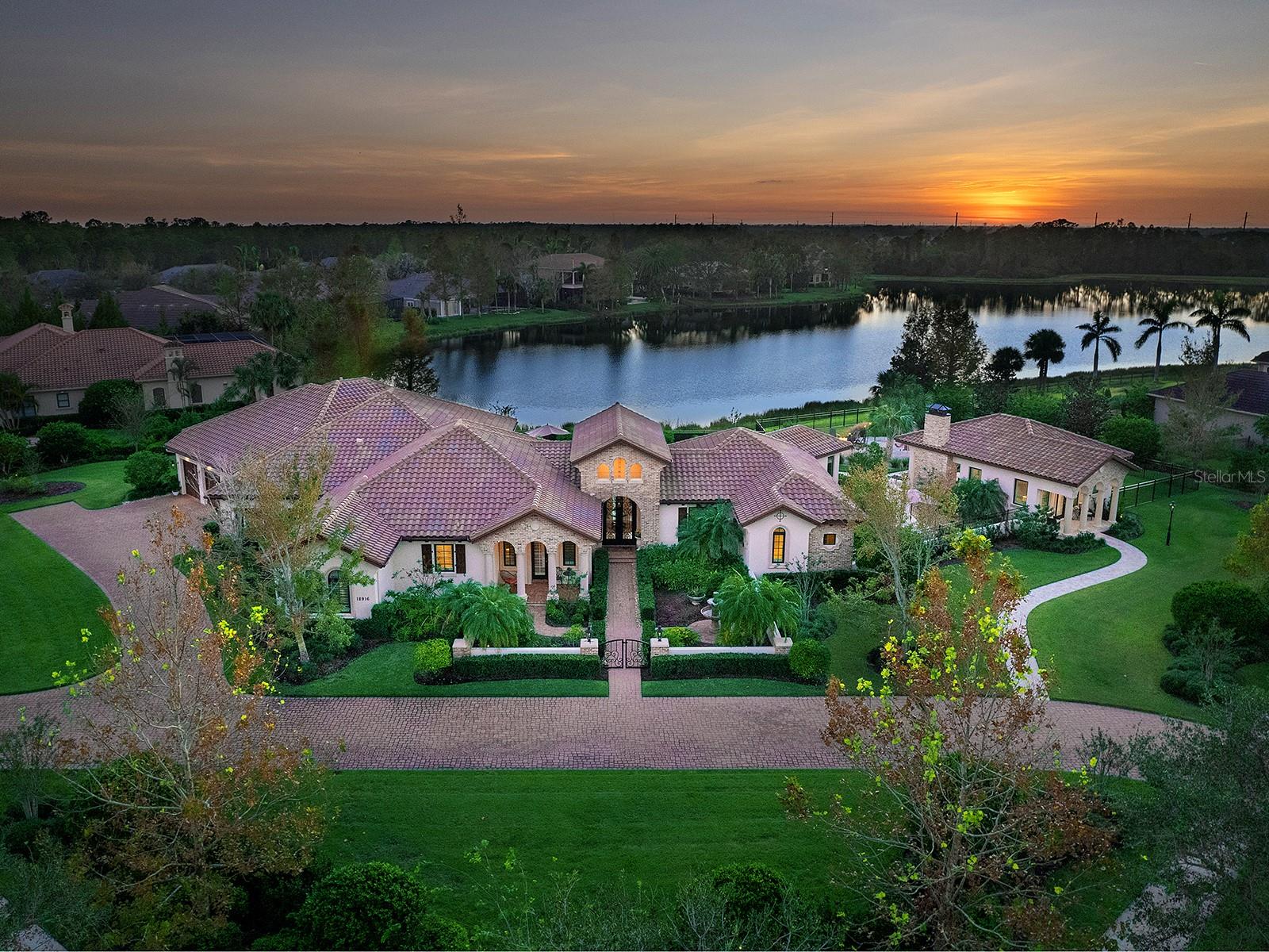 Exquisite custom estate is now available in The Concession, home to the world-renowned Jack Nicklaus and Tony Jacklin designed golf course. This private oasis is nestled along gorgeous lake views, and graces over 1.2 acres on a desirable corner lot, giving this home the perfect position to take advantage of sunset views over the lake. Built in 2015 by Anchor Homes, no detail in this luxurious estate has been overlooked, from the oversized 4-car garage to the open-air pool and lanai, gorgeous main home, or the just completed 2024 guest house. Arrive home via a large semi-circle driveway, lush landscaping, elegant front gate and welcoming courtyard with fountain. Enter through double iron and glass front doors, you will be immediately impressed by the spacious foyer with volume ceilings and immediate views outside. Relish in the warm details throughout this residence including architectural columns, chiseled travertine flooring, custom ceilings, brick facades, and plentiful bright windows overlooking the lake. Elegant archways set apart the formal dining room, with a dedicated wine room, from the casual dining area next to the chef’s kitchen. Enjoy creating meals with a stainless-steel appliance suite featuring Wolf gas range, central island, and cleverly hidden refrigerator, dishwasher and spacious walk-in pantry. The mix of textures and natural elements throughout is highlighted by the brick range hood, warm stone counters, and is carried into the great room with exposed wood beam vaulted ceiling. From the great room’s French doors, you can bring the entertaining outdoors to the covered lanai where you can enjoy cozy evenings around the fireplace or grilling at the outdoor kitchen. The highlight of the lanai is the sparkling pool with raised spa, stepping-stones and hidden rock speakers overlooking the lake. The fenced backyard has upgraded landscaping and hardscaping throughout to create several private areas to relish in the outdoors, including a gate separating the pool area and casita lanai, separate firepit area with lake views, and a private pathway to the courtyard picnic space. Inside there are multi-functional rooms perfect for every lifestyle with a large bonus (game or media) room, “card room” off the bonus room with tented ceiling, full pool bathroom, study, and laundry with oversized storage room. Your private primary wing showcases a large bedroom, separate seating area perfect for morning coffee, dual walk-in closets with custom shelving, and an elegant vestibule entry. The primary bathroom features dual vanities, freestanding tub and walk-in shower. Guests will enjoy their own accommodations with an en-suite guest bedroom, and two additional bedrooms with jack and jill bathroom. Whether you’re looking for space for multi-gen living, live-in care, or long-term guests, the detached guest house adds privacy. Featuring a private entry, lake views, bedroom, full bathroom, kitchenette, living room, and its own lanai with pizza oven, fireplace and firepit area. Peace of mind is secured with Anchor’s quality construction, impact windows and doors, and tile roof. The Concession is one of the most exclusive neighborhoods with less than 250 homes and private gated entrances. Memberships are available to the private golf club to enjoy the award-winning golf course, clubhouse and restaurant. Located mere minutes from Lakewood Ranch, enjoy the superb benefits of a flourishing community without the CDD fees!