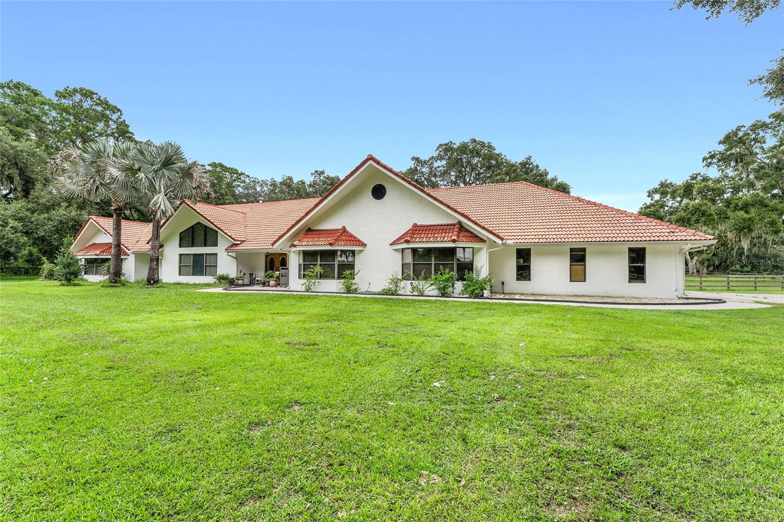 Welcome to your private estate in the heart of Florida’s renowned horse country. This exceptional 30-acre farm features rolling, oak-shaded pastures, fully fenced with board fencing and automatic waterers throughout, offering a perfect blend of beauty and functionality. A gated entrance ensures privacy, while the property remains just 20 miles from the World Equestrian Center and less than 10 miles from HITS.
The Mediterranean-style residence is built to last and perfectly situated among mature trees, providing a serene backdrop for both everyday living and entertaining. A large covered outdoor living area flows effortlessly to the screened pool deck, creating a resort-like setting for gatherings. Inside, soaring ceilings and abundant natural light welcome you, while the living room serves as a true centerpiece with a floor-to-ceiling stone wood-burning fireplace and custom 12-foot-high oak bookshelves. The kitchen is thoughtfully designed with granite countertops and a built-in oven and microwave, combining both style and function for any culinary occasion.
The primary suite is a private retreat, complete with a generous walk-in closet and a spa-inspired ensuite bathroom with an electric fireplace and a luxurious tiled walk-in shower. Additional conveniences include a mudroom off the garage with interior laundry and its own shower, perfect for rinsing off after a day in the pastures.
The farm features a functional custom show barn with an inside wash rack, on-site laundry, palpation rack, automatic fly system, 4 foaling stalls, 6 spacious 12x12 stalls, and two tack rooms. Attached to the barn is a 1-bedroom apartment with a full kitchen, offering flexibility for guests or staff. Additional amenities include a spacious workshop and an RV hookup!
This property perfectly captures the essence of Florida horse country living, combining enduring craftsmanship, timeless elegance, and practical equestrian facilities in a private, tranquil setting.