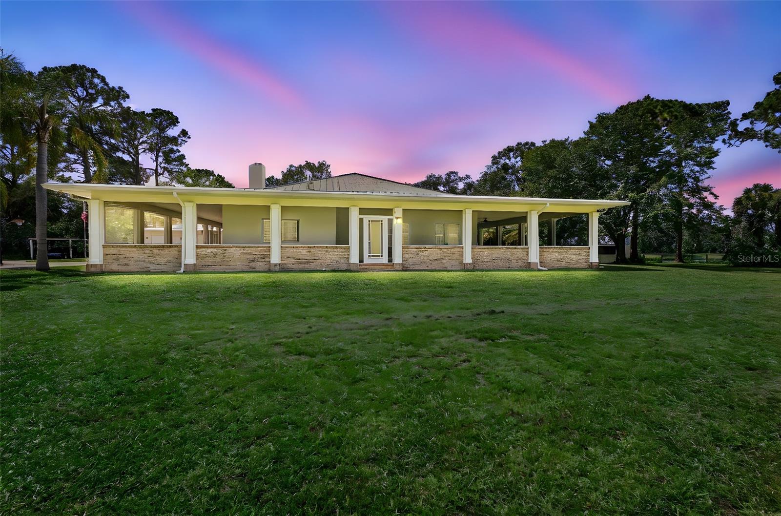 Opportunities to own a property of this distinction are few and far between- this is your chance to acquire one of the most unique and exceptional properties in all of New Smyrna Beach. As you arrive, you’re welcomed by a stunning hand-laid brick paver driveway, gracefully bordered by tall manicured hedges. The drive opens to a grand roundabout centered by a flagpole, setting a tone of classic elegance and timeless pride. Set on 2.66 picturesque acres of cleared, fully fenced, and meticulously maintained land, the home is framed by a custom-designed, 4,000 square foot wrap-around screened-in porch, offering both presence and purpose. This tiled, fully screened space is accessible through nine sets of French doors, blurring the line between indoor luxury, and outdoor tranquility and creating a combined living space of over 7,000 square feet. Inside, the home continues to impress with soaring 12-foot ceilings, detailed crown molding, and real hardwood flooring throughout. The heart of the home is the expansive family room, anchored by a stately wood-burning fireplace with its grand mantle, creating an inviting space for relaxation and entertaining. The chef’s kitchen features granite countertops, a gas range, prep sink, and ample space for gathering and making memories. Just off the main living area, a secondary family room with custom built-ins offers the perfect spot for showcasing treasured collections or creating a cozy media space. Each bedroom is a private retreat, complete with its own en-suite bathroom and direct access to the porch via French doors- ideal for enjoying early morning coffee or peaceful evening sunsets. The primary suite is a true sanctuary, featuring a spacious bedroom with a connected office that could double as a library, a spa-inspired bathroom with a freestanding tub, dual vanities, and a generous walk-in closet. From nearly every angle of the home, you’re treated to views of mature pines and the tranquil pond, creating an atmosphere of seclusion and serenity. Outside, a brick-lined courtyard is surrounded by a breezeway to the oversized two-car garage, and a secondary gated entrance off the adjacent dirt road provides convenient access for trailers, large deliveries, or additional guest parking. This property is an equestrian’s dream, with ample space for cross-fencing, and a rear storage barn that could easily be converted into horse stalls and a tack room. Combining elegance, functionality, and a rare connection to nature- this home is more than a property, it’s a lifestyle. Don't miss the opportunity to make it yours.