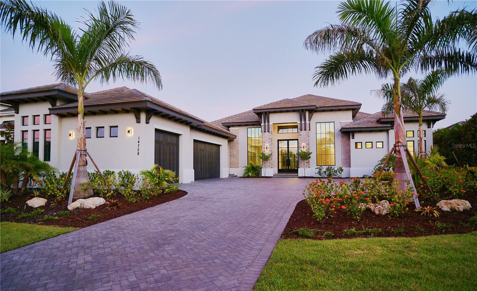 Transitional West Indies Custom Home by John Cannon Homes.
Experience the perfect blend of West Indies architecture with contemporary influences in this brand-new, never occupied custom residence. From the moment you arrive, huge tandem windows, a striking 10-foot custom iron entry door and a symmetrical façade draw your eyes straight through to the breathtaking rear views. Inside, the cathedral ceilings with scissor beams in the great room flow seamlessly to the main lanai and through the expansive pool enclosure. 10-foot accordion stacking doors topped with transom windows open the home to true indoor–outdoor living. A gas fireplace with cultured stone surround and mantle creates a warm focal point, while a climate-controlled wine room with illuminated agate stone panels adds an element of artistry. The home offers both a primary kitchen and a chef’s prep kitchen, each outfitted with high-end appliances. Natural light floods the space through an interior/exterior window and skylights. Two secondary bedrooms each feature en suite baths and walk-in closets. A versatile bonus room includes a disappearing corner door to extend entertaining space to the outdoors. In the owner's wing, you’ll find dual owner’s baths and closets—each closet with LED pin lighting and custom built-in cabinetry. A private owner's courtyard with outdoor shower and composite decking creates a resort-like retreat.
The rear lanai is fully equipped with an outdoor kitchen and island, overlooking the stunning pool area enclosed by a clear-view screen and colonnade. The pool features shellock pavers, a large sun shelf with cascade bubbler, in-pool lounge chairs, and a floating fire pit with mirrored granite edges. The negative-edge spa with glass waterline tile completes the scene. This smart home comes pre-wired for electric window treatments, and includes an integrated camera system, home music, and more—delivering luxury, comfort, and technology in one extraordinary package.
