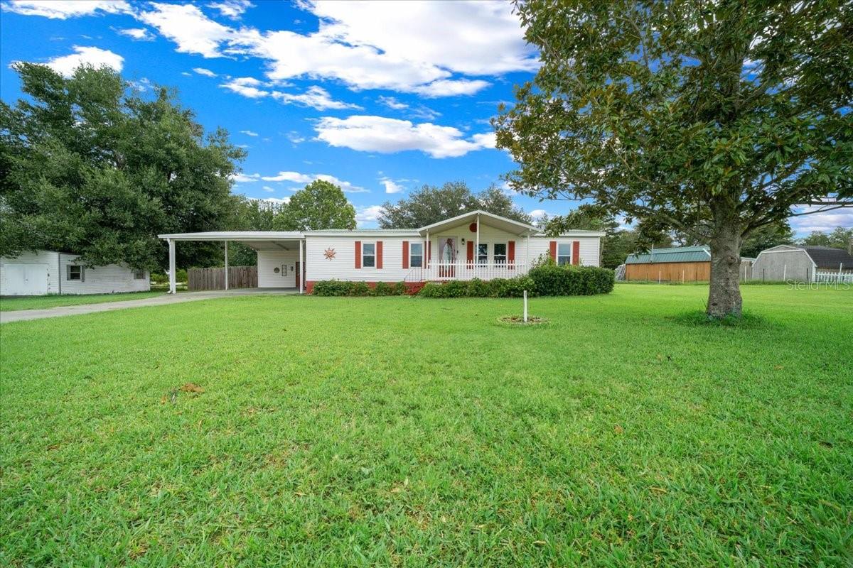 Welcome to this charmingly renovated and well-maintained home sitting on OVER a half an acre in Lady Lake, only a short golf cart ride away from all the amenities that The Villages has to enjoy without the HOA fees/restrictions! Take a drive down the extended driveway and pull under the carport for added convenience. Whether you choose to enter through the side door beneath the carport or step onto the inviting front porch and through the main entrance, you’re stepping into a home that seamlessly blends comfort, charm, and thoughtful design. Inside, you’ll discover a spacious split floorplan with laminate flooring throughout, and a stylish galley kitchen featuring modern cabinetry, generous counter and cabinet space, new appliances, and a convenient wet bar with a second sink, perfect for entertaining and everyday function. An inviting primary suite features a large walk-in closet and a beautifully updated en suite bathroom with double vanities and a spa-like shower complete with a built-in sitting bench. The secondary bathroom offers a classic shower/tub combo. Also included in the laundry room are a washer and dryer, storage cabinets and a storage closet. Additional highlights include a newer HVAC system, approximately five years old, and a brand-new water system, offering comfort and efficiency for years to come. Outside, the home continues to impress with a metal roof, a lush green front and backyard, a gorgeous mature magnolia tree in the front, and a large shade tree in the fenced backyard, perfect for pets, play, or peaceful relaxation. Step through the French doors off the dining room to enjoy the wooden deck, ideal for outdoor dining or unwinding in the fresh air. Enjoy your mornings on the covered front porch and evenings on the expansive covered rear patio. Attached to the carport is a versatile shed equipped with electricity, built-in shelving, lighting, a window, and a roll-up shutter door, perfect for storage, hobbies, or use as a functional workshop. Conveniently located near shopping, dining, and daily essentials, this Lady Lake gem is move-in ready and waiting to welcome you home.