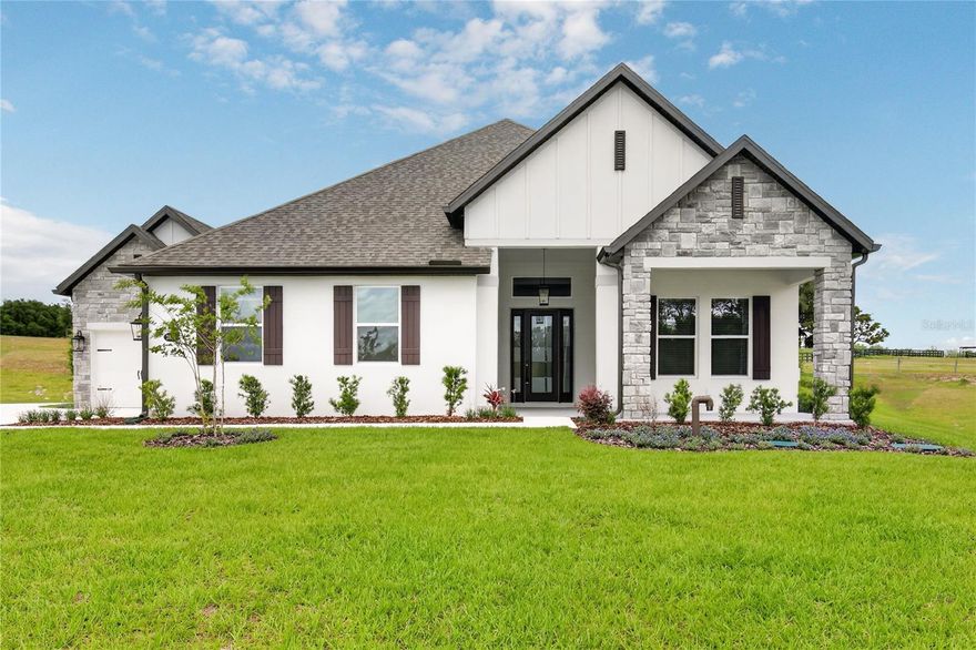 Welcome to Waycross, a spacious and thoughtfully designed four-bedroom, three-bath home with a three-car garage, located in the new Saddle Hill community in Fruitland Park. From the inviting covered front porch to the wide, welcoming foyer, this home offers a seamless blend of comfort and functionality. The open-concept layout features expansive main living areas, where the family room, kitchen, and breakfast area flow together effortlessly—ideal for everyday living and entertaining. The kitchen showcases a large breakfast bar, walk-in pantry, quartz countertops, bright white cabinetry, stainless steel appliances, modern tile backsplash, and matte black hardware. A separate dining area provides additional space for formal or casual gatherings. French doors open to a covered outdoor kitchen, extending the living space and creating an ideal setting for outdoor relaxation or entertaining. A dedicated media room offers flexible space for a home theater, game room, or additional living area. The primary suite is located at the rear of the home for added privacy and features a spacious bedroom, spa-inspired bathroom with soaking tub, walk-in shower, and a large walk-in closet. Secondary bedrooms are well-positioned to provide comfort and flexibility for family or guests. Saddle Hill offers a peaceful, tree-lined setting while remaining conveniently close to shopping, dining, recreation, and everyday amenities. Enjoy nearby Lake Griffin, local golf courses, and the charm of surrounding communities.