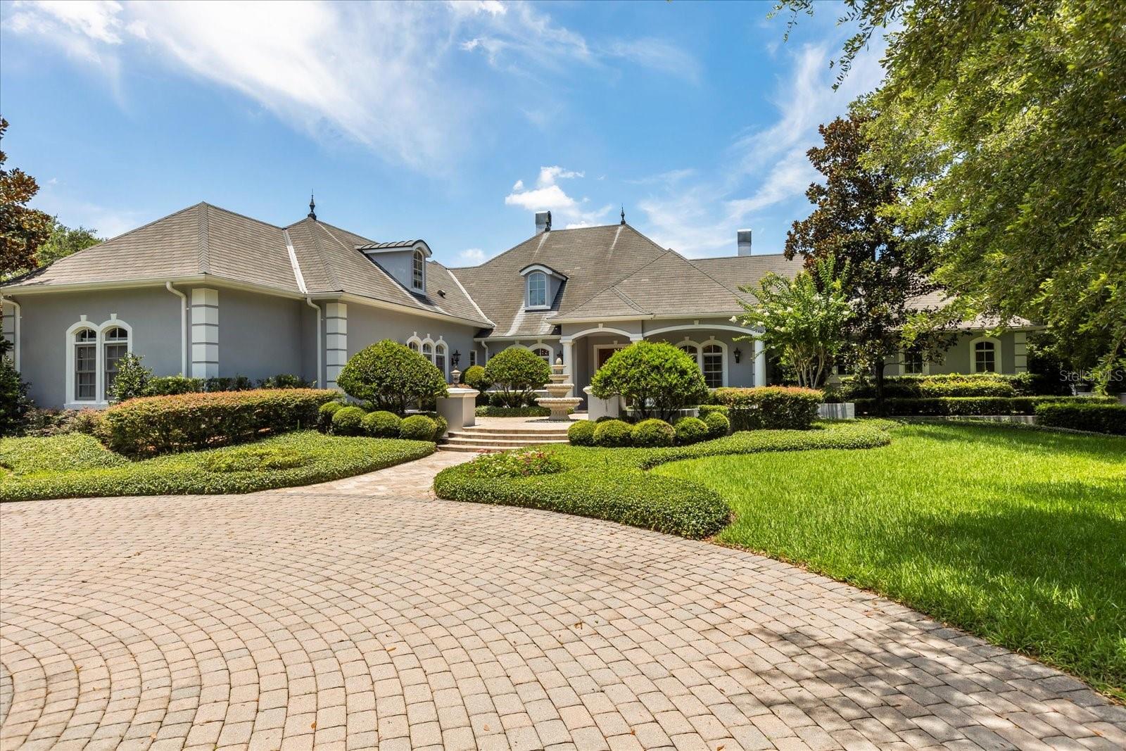 Discover luxury living in this stunning custom-built, lakefront estate nestled on a private gated lot along the tranquil shores of Lake Hill. Spanning over 6,700 sq ft of heated living space and nearly 9,640 sq ft total, this three-story single-family home offers refined comfort, timeless craftsmanship, and breathtaking panoramic water views.
The main level features a grand foyer leading to formal dining and a private office—both showcasing crown molding, built-in cabinetry, and elegant architectural touches like the stained glass interior window in the office. The living room boasts a cozy fireplace, lake-view balcony access, and stairs descending to the expansive lower level. The chef’s kitchen is fully equipped with a center island, pot filler, stainless steel appliances, ample counter space, and a charming breakfast nook.
The primary suite is a true retreat with crown molding, walk-in closet, and a luxurious en-suite bath complete with a dressing room, dual vanities, soaking tub, walk-in shower, bidet, and built-in storage. Additional main-level highlights include a spacious laundry room with a sink, walk-in wash tub, and plenty of cabinetry.
On the lower level, enjoy a large den with fireplace, wet bar, built-in entertainment center, and flexible space for recreation or entertaining. Two generously sized bedrooms on this floor feature en-suite baths, crown molding, and direct access to the rear patio.
The upper level attic presents a versatile bonus room—perfect for a home gym, media room, or additional bedroom.
Outside, the estate features meticulous landscaping, a circular drive, a 4-car oversized garage, and multiple outdoor living spaces to take in the serene lake views. This home is truly a private oasis—ideal for those seeking space, luxury, and lakeside serenity just minutes from Orlando conveniences.
