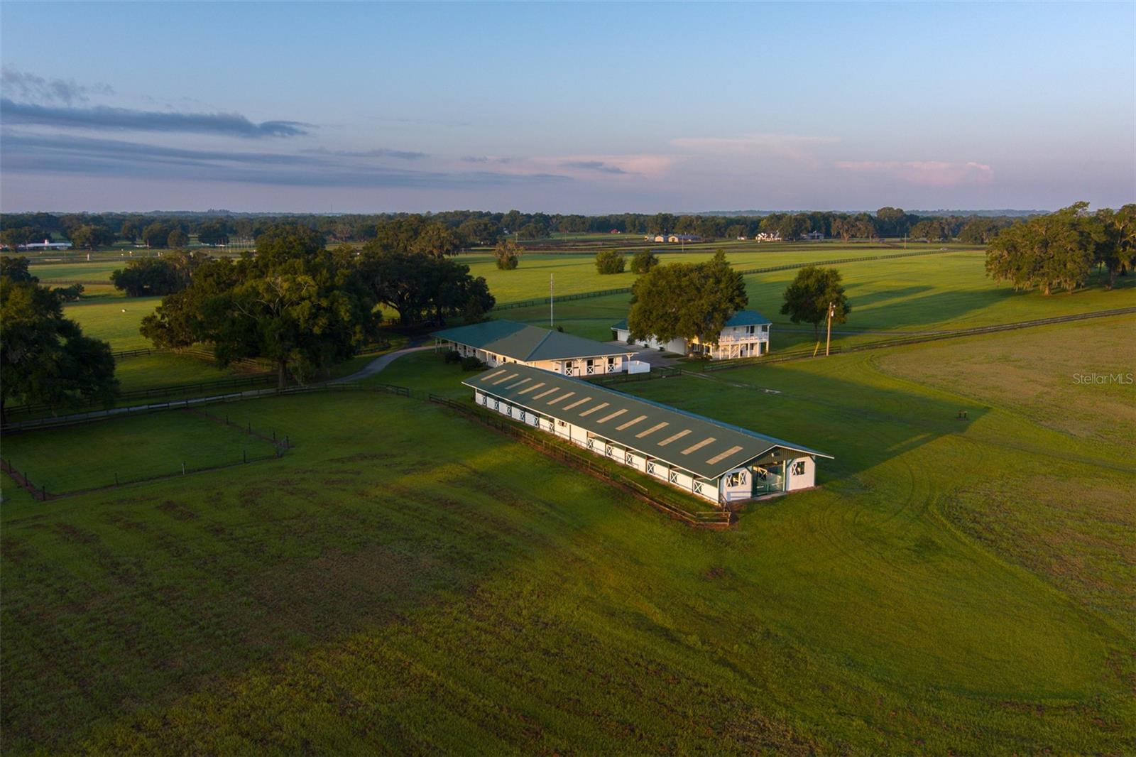 One of 2 contiguous parcels that make up Oak Lane Farm, this property personifies the Ocala horse country landscape with its rolling green pastures, grandaddy oaks, and a plethora of wildlife. With 165 acres, you will have your own private horse park. Riding the gently rolling fields and woodland trails under the farm's "big skies", is so peaceful and yet exhilarating, you will not want to leave. Should you decide to venture out, this farm is truly the epicenter for all Central Florida has to offer. The esteemed World Equestrian Center, as well as Ocala and Gainesville can all be reached in 30 minutes or less; the new WEC at Ocala Jockey Club is just 5 miles away. Major airports and both the East coast with available beach horseback riding, and the West Coast, are all day trips. This farm includes the Oak Hammock House which provides 2 ensuite bedrooms, 2 additional bedrooms, and one additional bath. There is also a 2 BR/4 BA Clubhouse, which features a great room, open bar with seating for 7, dining area, kitchen, and upstairs loft. This is a fantastic place to hold events, and entertain in a spacious, functional, and fun setting that provides panoramic views. The carriage house provides an office and a studio with 1/2 bath and laundry on the first floor, and a 2 BR/1 BA apt on the second floor. There is a 12-stall barn with an open central area for grooming, drying and saddling. It also features matted 12x12 stalls, wash rack, equipment storage and workshop, a garage, and a 2-story apartment with windows overlooking the stalls. There is also a 24-stall center aisle barn w/feed and tack rooms, wash rack and hay storage, and a large 4-bay equipment building. Electric and board paddocks serve both barns. Adjoining acreage is also available.