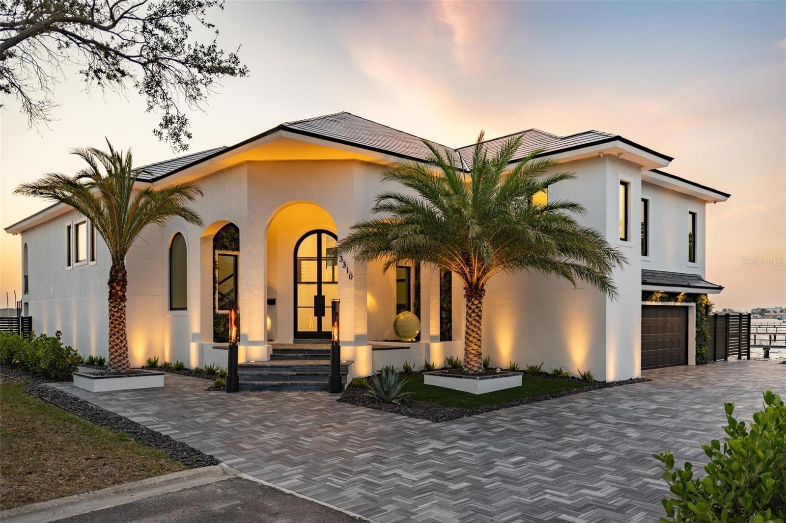 Set on a corner lot with over 200 feet of waterfront, this stunning all-block home was built by renowned St. Pete builder Tom Pici & Son and fully renovated—inside and out—over the past five years with no expense spared.
Every inch of the property is professionally landscaped and manicured. Over 7,300 sq ft of imported Italian marble was meticulously installed by Paramount Stone. Premium architectural and landscape lighting by Haven Lighting can be customized in elegant or vibrant color combinations. Tranquil water orb fountains enhance the outdoor ambiance.
A 12-foot arched, hurricane-rated front door framed by Vistafolia greenery welcomes you. Inside, the upstairs main living area features high ceilings and expansive water views. All windows were replaced in 2025 with PGT Winguards with Graylite II impact glass.
The chef’s kitchen includes Viking and Subzero appliances, high-end quartz countertops with waterfall edges, and a marble backsplash. The living room features massive sliding glass doors, floating shelves, custom cabinetry, a mist fireplace, and coffered ceilings.
The spacious primary suite has a large sliding glass door, a sleek microcement shower, and a custom walk-in closet. The upper level also includes two generously-sized bedrooms with custom closets, two more luxurious bathrooms, a large butler’s pantry with well-appointed laundry with built-ins.
An elevator services all levels. The lower level adds 2,000 sq ft of air-conditioned living space with a full bath, kitchenette, Naturekast cabinets, quartz counters, a large room (ideal as an office or guest suite), and abundant open space for a gym, game room and lounge. The custom media room includes a 175” acoustically-transparent screen, pre-wiring for 15-channel Atmos, and in acoustic treatments.
Outdoors, over 2,000 sq ft of waterfront covered patio space borders a 37x22 ft custom pool and oversized spa, positioned to enjoy views of John’s Pass and Boca Ciega Bay. The pool has a smooth Pebble Breeze finish, a Pentair heat pump, and a propane gas heater powered by a 500-gallon buried tank. Fifteen Halofire torches add drama, while a putting green, and lush lawn were done by Modern Grounds.
The modern seawall was reinforced with 240 tons of limestone riprap during the pool construction. All three AC units were replaced in 2022; the attic was re-insulated in 2024 and the upstairs ductwork redesigned. The whole house utilizes softened and carbon-filtered water with heated and chilled reverse osmosis water in the kitchen. Generous parking for 3 cars in the immaculate 819 sq ft garage complete with epoxy floor and pre-wired for EV charging.
A 34 kW Tesla Solar Roof with four Powerwall batteries offsets roughly in annual energy costs.
The composite dock features Azek decking, Durosleeve pilings, and a 13,000 lb Neptune G3 lift—for a center console. Frequent visits from dolphins, manatees, rays, and birds complete this extraordinary waterfront lifestyle.