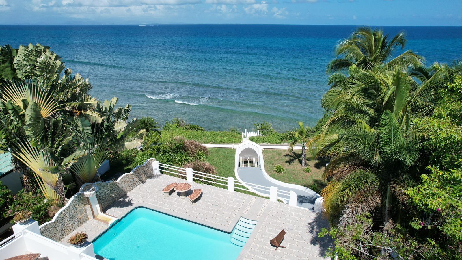 Villa La Riposa is beachfront living at its best. This amazing oceanfront property sits on a large lot that extends between two streets in the exclusive Bravos de Boston neighborhood. The property is bounded by the north shore beaches and is a 15 min walk to all the commodities in Isabel II (the ferry, restaurants, shops, and markets), and just 15 minutes from the airport (by car). It’s promontory location gives the property a sense of seclusion and allows for unobstructed 180 ocean views.
The art deco style villa elegantly mixes Mediterranean and Caribbean architecture. It’s distinct blue dome has become iconic of the North Shore skyline. The most spectacular space is the upper level apartment which has a unique European vibe with its stone mosaic floors, cathedral-esque arches, and grecian style louvered cabinets. The back drop from the main living space and the large outdoor lounge are the magnificent pool and turquoise ocean. Some of the spaces best features are the exterior bathroom and the amazing rooftop duomo with views of the mainland, Palomino and Culebra. Its doric columns frame the spectacular sunrises and sunsets during the morning and evening hours and the ferries can be seen as they come and go during the days.
The lower level apartments each are fully equipped and have their own outdoor spaces and separate entrances. Guests can enjoy a private dinner or evening in but come together for gatherings in the large garden terrace that surrounds the pool and fountain.
All the spaces are interconnected and have access to the ocean with a natural tide pool via a stairway built into the rocky cliffside. Every room has it’s own AC unit. The villa also has a parking area for up to three cars and additional private street parking, outdoor storage, and an outdoor shower by the pool area. The villa can be a great home, vacation escape, or an income producing rental.