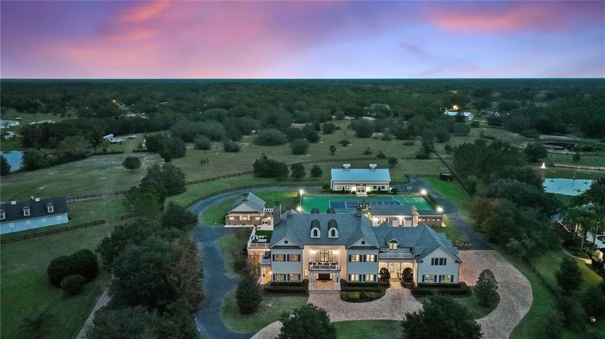 This home isn’t for the faint of heart … it’s a showstopper.  
Just under 14,000 ft.², 5 buildings, 13.75 neat & tidy acres in the double gated enclave of Mills Cove. 30 mins to DT Orlando, less than an hour to the beach, 10 minute helicopter ride to the airport, yet you’ll feel like you’re on your country estate.
The quintessential entertainment home radiates quality with a hyper-luxe moment around every bend. The undeniable quality of this developer’s personal dream home, is evident from the moment you cross the threshold into the 2014 Parade of Homes Custom Showcase GRAND AWARD WINNER by Hill Gray Seven’s Gregg Hill.  
Set back an acre, guests are greeted in neo-colonial style, with the pomp & circumstance one expects for heads of state. Travel around from either gate, to the front stone entry or round either corner to the property edges, then head back to the two bedroom guest cottage w/ stable beyond, or (on the other side) past the sports complex/tennis/pickleball/basketball courts to the stables. 
Saunter in from the grande front portico and you’ll be transported to an era when hospitality, ease & decorum were to be expected.  
Once inside, you’ll be warmly welcomed by a 2 story entrance gallery flanked by (4) 13’ double arched custom mirrored niches. Left to the 2 story, wood paneled study & fireplace w/separate entry, a British inspired sports pub/trophy room, a powder room w/hand laid marble mosaic tiles. 
Head right you’ll find the Fibonacci-esque spiraling staircase anchored by the game playing studio. 
Entertainment meets unencumbered formality.  The grande living room, fireplace & hearth is opposite the kitchen w/ triple thick rockface edged slab, 12’x 16’ kitchen continent. Sweeping views of the resort sized aquatic playground just beyond.  Kitchen adjacent are breakfast & wine tasting rooms, showcase pantry, craft room, 2nd powder room, mud room, doggy bathroom (w/shower, separate tub, washer/dryer & pups potty access). The sunroom hosts formal dining & music conservatory anchored by it’s weighty brick fireplace & hearth.  
Upstairs, the primary bedroom, faux turf deck for lounging, improving your putting game, or surveilling your dominion.  The primary bath is a work of art with hand laid leaf marble mosaic tile harkening to the 11th century Moorish Maallem’ craftsmen.
3 en-suite bedrooms, a bunkhouse, billiards room, home theatre, 2 additional turfed decks, a 3rd story bonus room provide space for everyone to “do their thing”.  A 2nd staircase, provides additional access & flow.  
The pool accommodates your entire guest list, sunken summer kitchen & swim up bar serves meals under sunny skies, or sur la nuit étoilée. A 2 bdrm guest cottage w/ kitchen & fireplace keeps guests comfy & well accommodated.  Fitness studio overlooks pool & tennis courts, tennis viewing platform easily seats 12.  The freestanding yoga/dance studio adjoins the tennis courts and al fresco lounging patio is an ideal vantage point to watch a good match. The payoff for good workout is a relaxing aromatherapy steam shower. The 5 stall aisle barn & tack room is immaculate, grooming stations, trainer’s studio apartment, full length hayloft/storage. Paddock for turning out or a manège, cleared acreage behind the stables is for riding, establishing an orchard, or both.  
Familiar and comfortable, even the deer feel relaxed here, meandering without hesitation.  So will you. 
Broker is Lic'd Real Estate Agt. MLS details to be verified by buyer