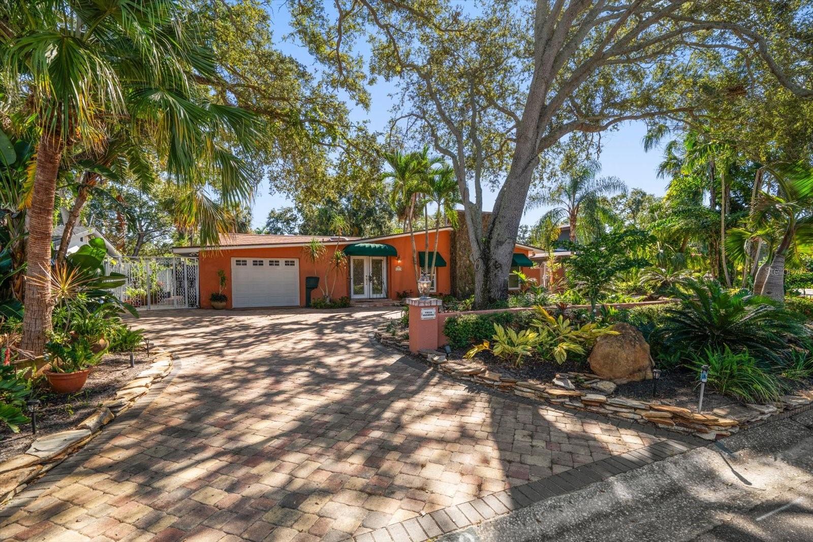 Welcome to VILLA HERMOSA—a hidden gem tucked away in the highly sought-after Jungle Prada neighborhood on Florida’s west coast. This private, one-story retreat offers a rare combination of timeless design and casual coastal living, featuring 3 bedrooms, 2 bathrooms, 2,206 square feet of elegant indoor space, and an oversized attached garage—all set behind ornamental iron gates on a lushly landscaped lot. From the moment you arrive, a sense of serenity sets in. A circular paver driveway, decorative column lighting, and double leaded glass doors welcome you home. Step inside to find a light-filled, open floor plan anchored by a warm and inviting living room with a fireplace and two sets of French doors. These lead to a spacious 13x30 screened side porch with a striking Sunburst design—perfect for seamless indoor-outdoor living. Just beyond is a peaceful side yard, ideal for meditation, sunbathing, or your morning coffee. Love to entertain? The private outdoor space is a standout feature of this home. Relax in the sparkling saltwater Pebble Tec pool with a soothing rock waterfall, or fire up the custom outdoor kitchen and bar, complete with a 4-burner propane cooktop. Whether you're hosting weekend BBQs, sipping sunset cocktails, or simply unwinding after a long day, this space was designed for both peace and gathering. Inside, the kitchen is both functional and stylish, featuring granite countertops, stainless steel appliances, a cooktop stove, double convection oven, built-in wine rack, glass-front wood cabinetry, vaulted ceiling, and a custom desk area. French doors open from the kitchen to the outdoor entertaining area, and a separate formal dining room with a chandelier creates the perfect setting for family dinners or holiday gatherings. The primary suite is a true escape with three closets and an ensuite, spa-like bath featuring dual vanities, soaking jet tub, granite counters, dedicated vanity space, and a skylight that fills the room with natural light. Two additional bedrooms offer direct outdoor access—one leading to a private garden and the other to the screened side porch—making them ideal for guests, a home office, or creative studio. The guest bathroom includes a skylight, walk-in shower, granite counters, and custom built-ins with beautiful stone tile flooring and walls. Recent upgrades include a new roof (2024), impact windows in the living room and primary bedroom, fresh interior paint, and a new pool pump. Additional features include a house generator, outdoor shed, and a dedicated gardening area in the backyard—offering flexibility and functionality for any lifestyle. VILLA HERMOSA is ideally located just 1 minute to Abercrombie Park, 3 minutes to the public boat ramp, 5 minutes to Tyrone Square Mall, and 7 minutes to the Gulf beaches, offering the perfect balance of privacy, accessibility, and laid-back Florida charm. Schedule your private showing today and step into the lifestyle you deserve at VILLA HERMOSA