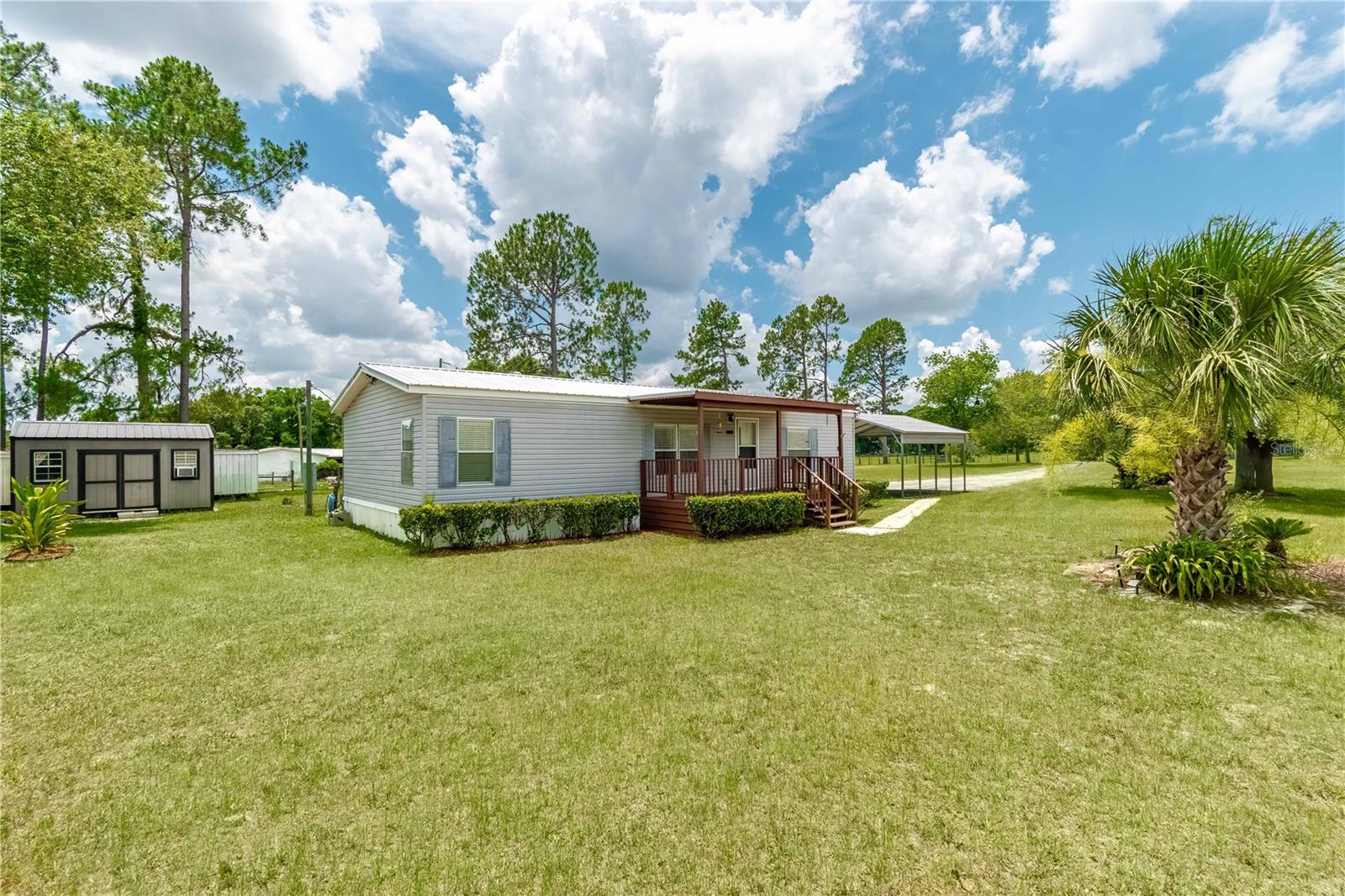 Tucked away within the tranquil Northwood Farms neighborhood and located just a short drive from both Gainesville and Ocala, this 1.26-acre property is the ideal blend of peaceful rural living and everyday convenience! Fully fenced with a gated entry, the land is high and dry with open ranch views across the road that creates an idyllic setting. The 3-bedroom, 2-bath double-wide home (2000 Merit) is move-in ready and features a practical split-bedroom layout with tile and wood laminate flooring throughout. The living and dining areas flow into a cozy country-style kitchen, and the interior laundry room (washer/dryer included) sits just off the kitchen for easy access. All major appliances were updated in 2023–2024, and a newer HVAC (2023) keeps the home comfortable year-round. Step outside to enjoy inviting outdoor living spaces: a covered front porch overlooking pasture views, a spacious 12' x 21' screened patio out back, and a firepit area to round out the backyard ambiance perfect for relaxing evenings or casual entertaining. There's plenty of space here for both people and animals to thrive, with plenty of opportunity to customize the property to further suit your needs. Additional features include a 20' x 20' metal carport (2022), a 10' x 16' utility/storage shed with a portable A/C unit (2025), and a large 8' x 40' metal workshop with multiple covered extensions for equipment or project storage. Many of North Central Florida’s natural attractions are just a short distance away, including Blue Grotto, Cedar Lakes, Devil’s Den, and many other, while equestrian venues like the World Equestrian Center (WEC), HITS, Black Prong, and Goethe State Forest trailheads are all within a 30 minute drive. Work in the city and live in the country– this property gives you the opportunity to enjoy the best of both worlds with no HOA!