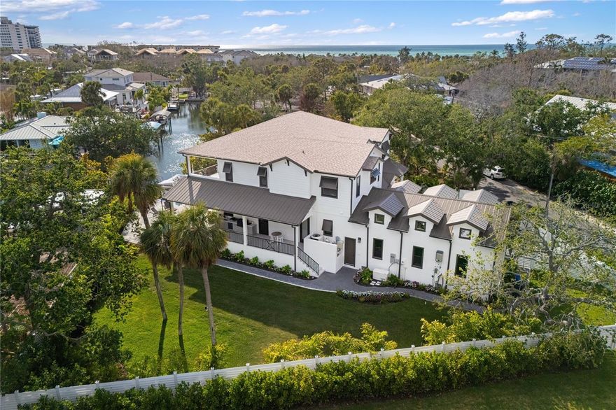 Start living your dream lifestyle on world-famous Siesta Key in this Pham Development custom-built waterfront British West Indies–style home. Located on a quiet street on the north end of the key—close to the beach, Siesta Key Village and Out-of-Door Academy—and just minutes on and off the island, this residence offers island living at its best. Set on a corner canal-front lot, the two-story home features 5 bedrooms, 5 full bathrooms and 1 half bath, with 3,875 square feet under air, a great room floor plan, soaring 22-foot vaulted ceilings, and walls of windows and doors—including large pocket sliders—that bring in abundant natural light and seamlessly connect indoor and outdoor living.

The adjacent dining area provides ample space for entertaining, while the stunning kitchen—completely open to the great room—serves as the heart of the home with a large 9-foot island with extended seating, professional stainless steel gas appliances and a walk-in butler’s pantry. The home also features a fully integrated security system, whole-home sound system and a complete Control4 smart home system. The first-floor owner’s suite offers a private retreat with a walk-in shower, freestanding tub, dual vanities, and a large custom walk-in closet. A laundry room, powder room and mudroom complete the first level, and a 3-car garage provides ample parking and storage.

Upstairs you’ll find four en-suite guest bedrooms, an additional laundry area to service them, and an expansive second-level balcony to take in the views. Outdoor living includes approximately 1,502 square feet of covered lanai, an exterior wrap-around porch, and balcony space designed for enjoying the island lifestyle, complete with SunBrite outdoor TVs, and Brazilian hardwood ceilings. The privately gated driveway and fully fenced property are surrounded by lush landscaping, creating a secluded tropical setting with a large swimming pool, champagne spa and expansive pool deck perfect for relaxing or entertaining. A private well supports irrigation. With 31 linear feet of canal frontage, the property features a 31-by-12-foot electric boat lift rated for 6,500 pounds, two jet ski ramps and about a 4.5-foot draft—ideal for boating and enjoying the water, making this oasis the perfect place to enjoy the Siesta Key lifestyle.