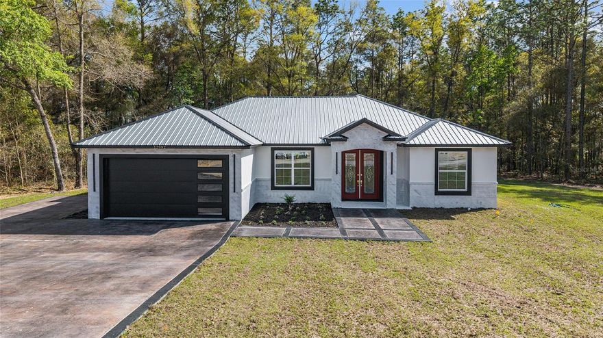 Welcome to your private slice of luxury living in Ocala! Situated on 1.16 acres, this stunning 4-bedroom, 3-bathroom home offers the perfect blend of modern design, functionality, and space to breathe. From the moment you arrive, you’ll be impressed by the sleek exterior, metal roof, and inviting entryway. Step inside to an expansive open-concept floor plan featuring soaring coffered (Crawford-style) ceilings, designer finishes, and gorgeous oversized tile flooring throughout the main living areas. The heart of the home is the chef-inspired kitchen, complete with a massive island, quartz countertops, custom cabinetry, high-end appliances, and eye-catching gold accents—perfect for entertaining or everyday living. The spacious living area features a modern electric fireplace, creating a warm and stylish focal point, and flows seamlessly into the dining space and outdoor access. This home offers two master suites, ideal for multi-generational living or guests. The primary suite is a true retreat with a spa-like bathroom featuring dual vanities, a large walk-in shower, and elegant finishes. Additional highlights include, Bright and airy bedrooms with ample space, Stylish laundry room with built-in cabinetry and sink, Designer lighting and fixtures throughout. Large windows bringing in natural light and serene wooded views. Enjoy the peace and privacy of your oversized lot with plenty of room to add a pool, workshop, or outdoor oasis. If you’re looking for modern luxury with space and flexibility—this is it!