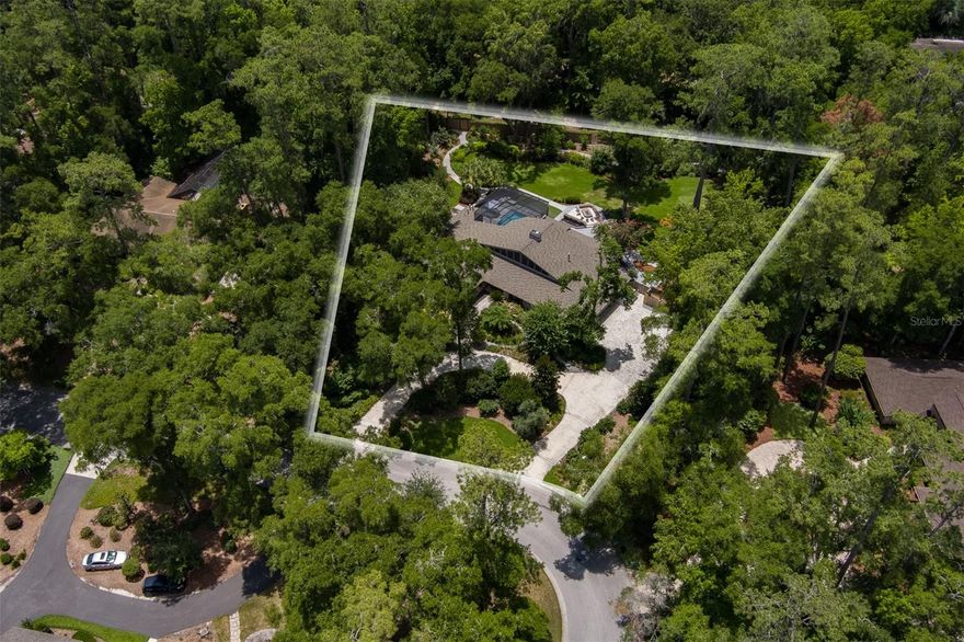 * * * * Spectacular In-town Retreat Near the University of Florida * * * * 
Nicely situated within the coveted Hermitage neighborhood, this architecturally distinctive residence sits on 1.1 acres of beautifully landscaped grounds, offering an exceptional combination of scale, serenity, and convenience. Meticulously updated, the home seamlessly blends design-forward sophistication with everyday comfort. ~ ~ 
Through double entry doors, a light-filled interior unfolds with travertine floors, soaring ceilings, and expansive walls of glass that blur the line between indoors and out. The great room—anchored by a dramatic fireplace—flows effortlessly through multiple living and entertaining spaces, including a custom bar with backlit quartzite, all overlooking the newly constructed (2025) resort-style pool and private backyard. ~ ~ 
The chef’s kitchen is both refined and functional, showcasing dual prep stations, a waterfall-edge island, steam and convection ovens, and sleek custom cabinetry. The tranquil primary suite offers a spa-like oasis with a relaxing soaking tub, oversized walk-in shower, and custom closet. A private secondary wing includes two bedrooms, a shared bath, a flex/media room, and a dedicated gym that could easily become an additional bedroom. ~ ~ 
Main Home: 4,272 sq ft + Studio Cottage: 288 sq ft // Total: 5,581 sq ft under roof ~ ~ 
Outdoors, the screened pool area is a true showpiece—featuring elegant water elements, a summer kitchen and grill room, full pool bath, multiple patios, fountains, a striking fire table, and a multi use design putting green. Winding garden paths lead through lush landscaping, fruit trees, and vibrant flowering gardens to the detached 1Bedroom/1Bath studio cottage with kitchenette. ~ ~ 
Thoughtfully designed exterior lighting creates a soft, elegant glow for daily enjoyment and transforms into a colorful, dynamic display for festive gatherings.
Smart home integration and a state-of-the-art security system offer intuitive control of lighting, climate, sound, and surveillance. Additional highlights include energy efficient impact-rated windows, solid concrete block construction, a spacious three-car garage, and additional half bath for evening guests, a spacious laundry room designed for 2 sets of washers/dryers with extensive storage—all just minutes from the University of Florida, top medical centers, premier shopping and dining, recreation and cultural venues that make Gainesville a fantastic place to live, work and play!
