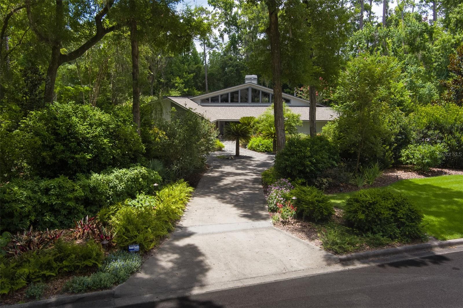 Architectural Sophistication on 1.1Private In-Town Acres~
Privately situated in the desirable Hermitage neighborhood, this architecturally distinctive residence on 1.1 beautifully landscaped acres offers a rare blend of scale, serenity, and convenience. Recently updated, this sophisticated property balances design-forward style with everyday elegance. ~
Enter through double doors to a sunlit interior featuring travertine floors, soaring ceilings, and floor-to-ceiling windows that seamlessly connects indoor and outdoor living. The expansive great room, anchored by a dramatic fireplace, flows effortlessly between multiple entertaining and living zones, including a custom bar area with backlit quartzite—all overlooking the newly-built (2025) resort-style pool and private backyard. The great room opens to the chef’s kitchen, as functional as it is beautiful, with dual prep stations, a waterfall edge countertop, induction cooktop, steam and convection ovens, and sleek custom cabinetry. ~
The serene primary suite offers a spa-like retreat with a soaking tub, large walk-in shower, and custom closet. The private secondary wing includes two bedrooms, a shared bath, a flex/media room, and a separate gym. Recent enhancements include new flooring, impact-rated windows and updated lighting that elevates both ambiance and energy efficiency. ~
Outdoors, a screened-in pool area is enhanced with water features and surrounded by a grill room with a summer kitchen, a full pool bath, multiple patios, fountains, a remarkable fire table, and a putting green. The park-like backyard private oasis is nothing short of magical - an illuminated garden path winds past a detached 1BR/1BA studio guest cottage with kitchenette, weaving through extensive landscaping, fruit trees, and a vibrant tapestry of flowering shrubs and greenery. ~ The exterior lighting is thoughtfully designed for versatility—offering soft, ambient illumination for everyday elegance, while effortlessly transforming into a vibrant, colorful display to elevate special occasions, festive gatherings, or celebratory events. ~
Equipped with smart home integration and a state-of-the-art security system, this home offers intuitive control of lighting, climate, sound, and surveillance. Additional highlights include a three-car garage, spacious laundry room, and concrete block construction—all just minutes from The University of Florida, top medical centers, and Gainesville’s finest dining and shopping. https://gainesville360.com/2025/2261/