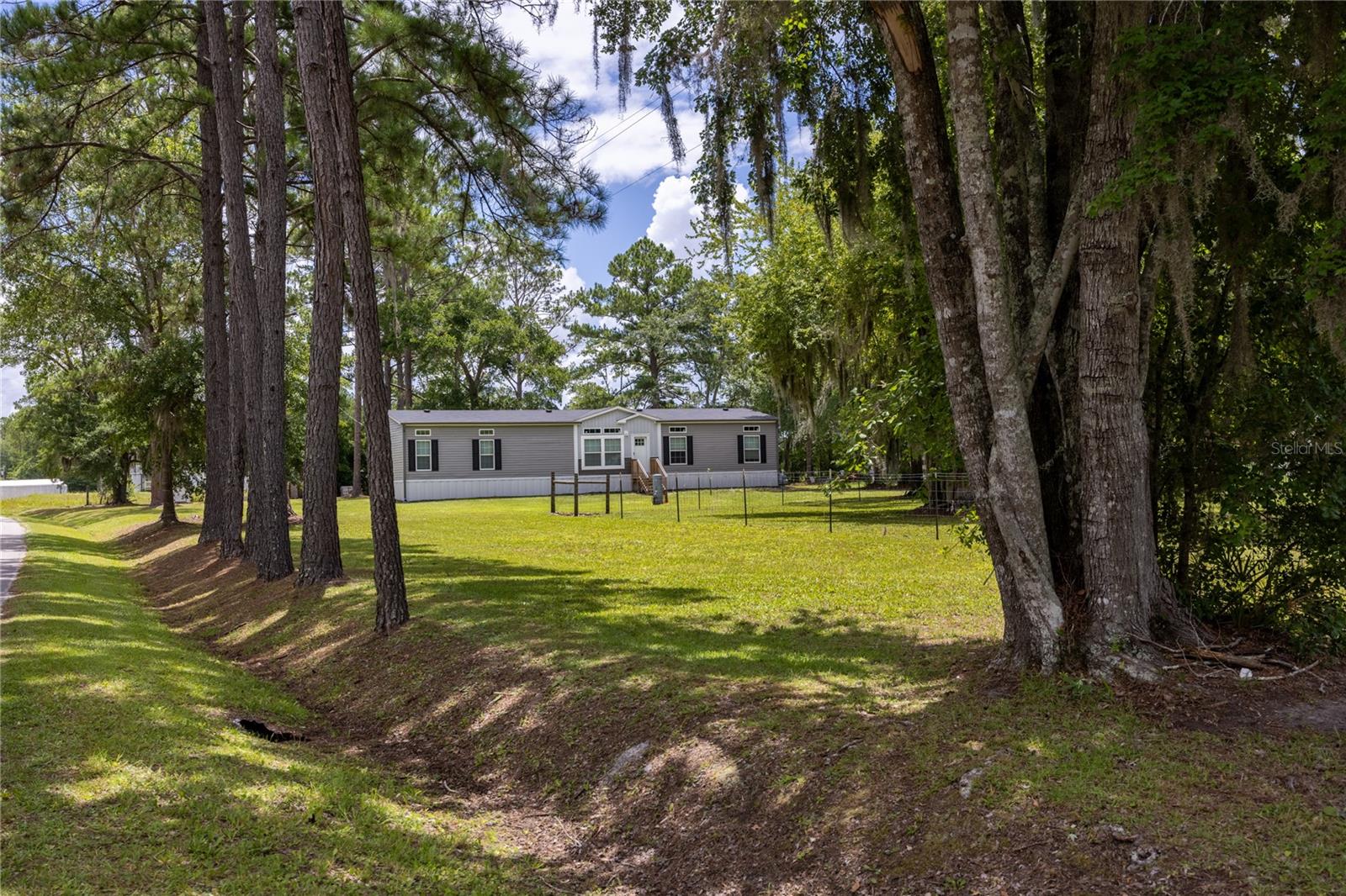 Don’t miss this incredible opportunity to own a like-new 4-bedroom, 2-bath manufactured home situated on just over an acre in scenic Columbia County. This 2023 lot model spans more than 1,800 square feet and is loaded with premium upgrades and custom touches that make it stand out from the rest. From the moment you walk in, you’ll notice the spacious layout, high ceilings, and thoughtfully designed floorplan that offers both comfort and functionality. The open concept living area flows seamlessly into the well-appointed kitchen and dining spaces, creating the perfect environment for entertaining or everyday living. The split-bedroom design ensures privacy, with a generous primary suite featuring a walk-in closet and a spacious en-suite bath. On the opposite side of the home, you’ll find three additional bedrooms and a well-appointed guest bathroom which provides plenty of space for family, guests, or a home office setup. Outside, you’ll find multiple outbuildings offering plenty of space for storage, hobbies, or workshop use, as well as a covered carport with a concrete slab that is ideal for vehicles, boats, or recreational equipment. The property offers the peace and quiet of country living while still being conveniently located to local amenities. This home is move-in ready! Schedule your showing today and see all that this beautiful property offers! **Property lines on photos are approximate**
