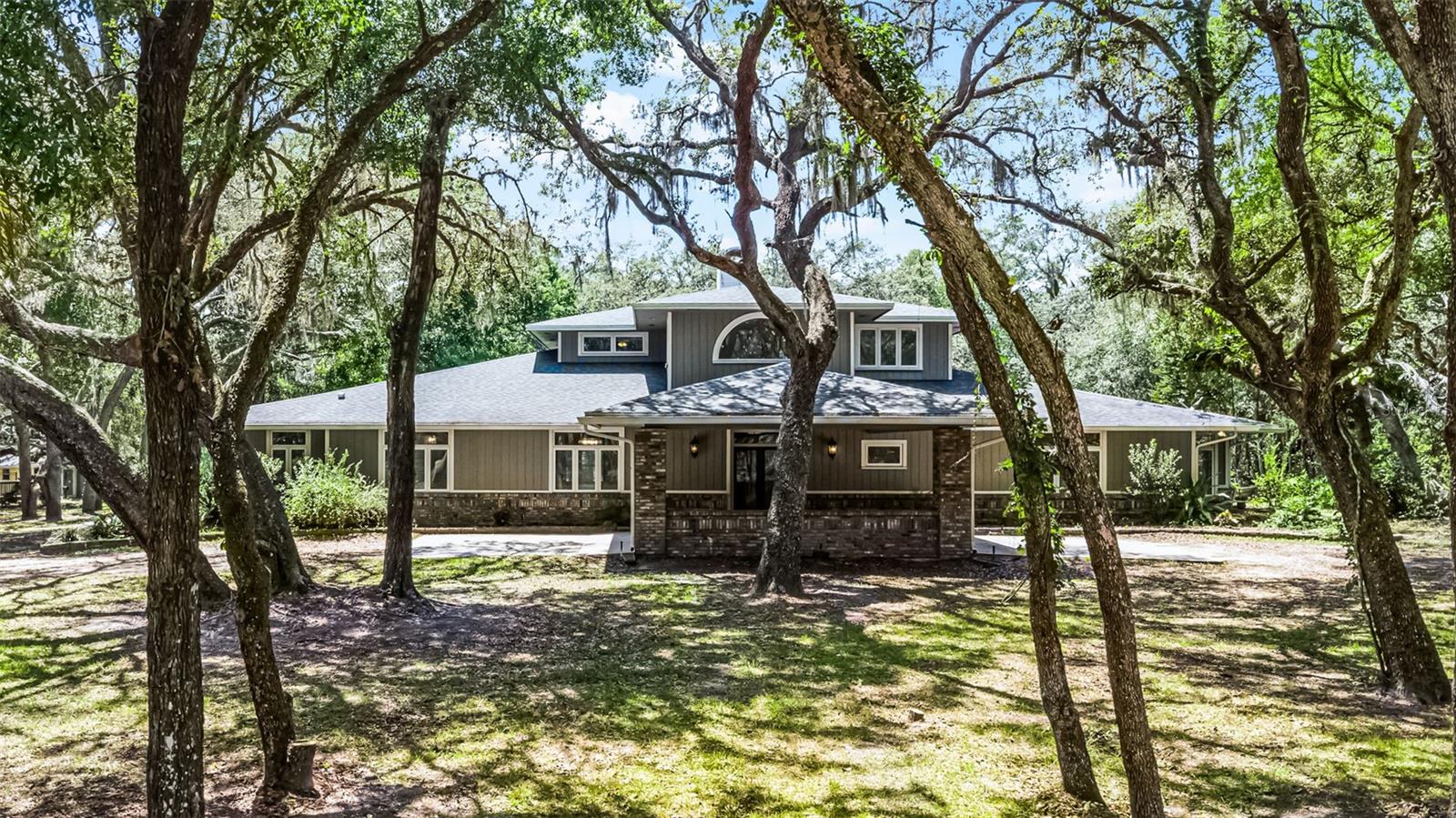 Welcome to 5655 Oak Hollow Lane, where the essence of Old Florida comes to life at the end of a quiet, private road. As you drive down Oak Hollow Lane—a peaceful dirt road where time seems to slow and the world feels far away—you’ll arrive at the gated entrance to a rare gem: a custom-built lakefront home nestled on nearly six acres of natural beauty and refined comfort.
Once inside the gate, the landscape unfolds with native Florida flora such as Saw Palmetto, Scrub Oak, Sabal Palms, and Beauty Bushes, setting the stage for a serene and secluded lifestyle. Wildlife abounds here—deer, wild turkeys, ducks, and the occasional eagle are regular visitors to spring-fed Lake Marie. Whether you're fishing from the dock, relaxing in the gazebo by the massive outdoor fireplace, or enjoying a quiet moment on the screened porch, this property invites you to reconnect with nature.
The main home features 4 bedrooms, 3 full bathrooms, formal living and dining rooms, and a spacious family room with a wood-burning fireplace. The well-designed split-bedroom floor plan includes a serene primary suite downstairs—a true owner’s retreat—with its own sunroom, spa-like bath, oversized walk-in closet, and direct access to the screened porch with stunning lake views. A second downstairs bedroom with a private entrance and full bath offers flexibility as a guest suite, home office, or den. Upstairs, two generously sized bedrooms share a modern Jack-and-Jill bathroom, each with large closets and picturesque views of the lake.
Entertain with ease in the grand foyer, where soaring 20-foot ceilings and a dramatic staircase welcome you from the expansive 27x22 porte-cochère. The gourmet kitchen is designed to impress, featuring a Sub-Zero stainless steel refrigerator, granite island, glass cooktop, walk-in pantry, wine cellar, and an informal dining area bathed in natural light. The spacious laundry room includes a farmhouse sink, abundant cabinetry, countertop space, and also serves as a practical powder room.
Step outside to the 82-foot-long covered and screened lanai with a heated spa and breathtaking views of the lake—perfect for year-round outdoor living. With over 200 feet of lake frontage, a sports court, two storage buildings, a fishing dock, and a floating dock, this property offers endless opportunities for recreation and relaxation.
Also included is a charming 2-bedroom, 1-bath guest cottage with its own screened porch, full kitchen, wood-burning fireplace, custom lighting, and private laundry. With its thoughtful design and stunning lake views, your guests may never want to leave.
At 5655 Oak Hollow Lane, you're not just buying a home—you're embracing a lifestyle. Welcome home... where your story begins at the end of a dirt road.