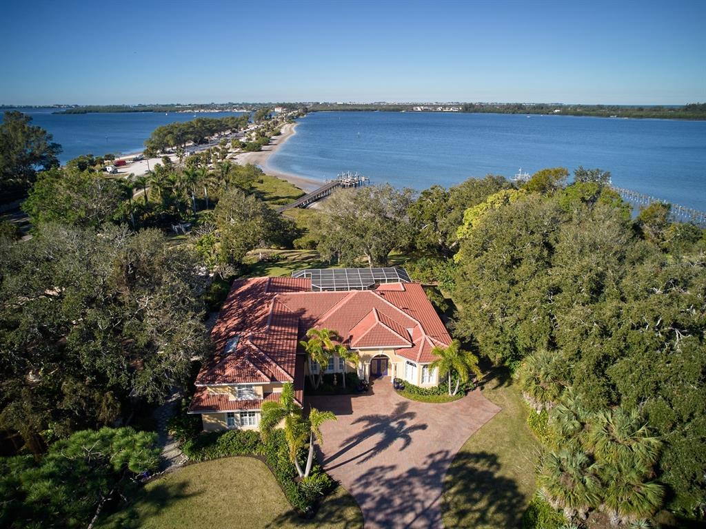 OPULENT 4,000+ SQUARE FOOT WATERFRONT ESTATE! Situated directly on Palma Sola Bay, this graceful mansion indulges a luxurious lifestyle. Its private grounds highlight an impressive waterside setting. Behind double leaded glass front doors, a stately formal foyer presents a lavish 3 bedroom, 4.5 bath residence with a den/study. Within its interior, only the finest of fixtures and finishes are appropriate; wall-to-wall handcrafted woodworking, double crown moldings, designer ceiling hues, venetian plaster walls (imported from Firenze Italy), plantation shutters, recessed and accent lighting, architectural inspired windows and doors, plus polished-crushed Jerusalem stone floors set on the diagonal. A quintet of sliding doors set the stage with water vistas in the living room. Formal entertainment extends into the adjacent dining room. Nearby, the gourmet kitchen has pocket doors that discreetly maintain decorum as the guests enjoy the fruits of its labor. Brimming with top-of-the-line amenities like robust granite surfaces, furniture quality cabinetry with custom details, contrasting built-in storage, a divided apron sink, a patterned hand-set backsplash, and a walk-in pantry. There is a useful wet bar with a second smaller apron sink and display shelving. The center-island has a cooktop, storage, and bar seating. All state-of-the-art appliances remain and include a double oven and cabinetry paneled dishwasher and refrigerator. The stained-glass clerestory window is the flourish that caps off the space. Two sets of aquarium glass windows look out over the water views and allow natural lighting to cascade into the kitchen and informal dining area. Combined with the family room featuring a marble encased, gas fireplace. French doors open to the lanai and double doors close off the bayside den/study with its own paver patio. Conveniently close is a guest bath with access to the pool. A secondary en suite has a garden view behind French doors. Attached is a three-piece washroom and a large walk-in dressing room. The well-appointed laundry room, with entry into the 2-car garage, completes this side of the home. The opposite wing boasts a huge private Owner’s suite with a sitting area overlooking the water vistas. Matching fabrics cascade behind the furnishings and frame the windows. Double doors give way to a corridor with a walk-in closet, a secondary closet, and the distinctive bath. Boasting brass fixtures, dual sinks, solid surfaces, etched glass partitions, a lavatory equipped with a bidet, a claw foot tub, and a zero-entry walk-in shower. A hardwood staircase leads to the second level, also with wood floors that flow gracefully into another comfortable and private primary suite with a bath. Outdoor entertaining begins on the columned veranda with a screen enclosure extending over the heated saltwater pool and spa. Over a half an acre of pristine bay front is manicured expertly for a park-like setting that coexists with a natural habitat recognized for manatees, dolphins, sea turtles, wading birds, fish, and other wildlife. Palma Sola means solitary palm. A single ancient palm tree, still standing today at Holmes Beach, gives way to the designation of these bay waters by Sailors looking for the horizon of Anna Maria Island. The small embayment in West Bradenton opens to Anna Maria Sound. The fishing community of Cortez is just southwest, and Manatee County’s Robinson Preserve is to the north.