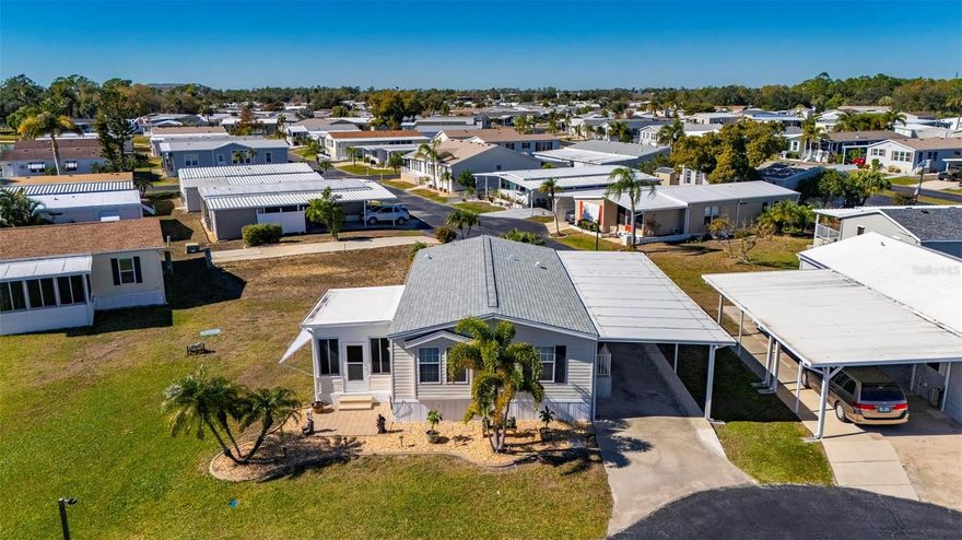 This beautifully furnished 2-bedroom, 2-bath LAKE VIEW manufactured home is located in a well-maintained 55+ co-op community and sits at the end of a peaceful cul-de-sac, offering added privacy and serene lake views. NOT IN FLOOD ZONE. The home has been extensively updated and features luxury vinyl flooring flowing seamlessly throughout, complemented by crown molding, double-pane windows, and Florida-style bimini shutters that enhance both style and energy efficiency. Major upgrades include a long carport added in 2024, a shingle roof replaced in 2023, and a complete HVAC system installed in 2022. The updated kitchen offers Corian countertops, ample cabinetry, and opens to a dedicated laundry room for added convenience. Both bedrooms are generously sized and provide abundant closet space. The enclosed lanai is a true highlight, overlooking the lake and creating the perfect space for year-round relaxation, while an additional paved outdoor patio just beyond the lanai offers an ideal setting for outdoor seating and entertaining. A 12x12 double-door shed with electric, installed in 2024, provides excellent storage or space for a golf cart. This move-in-ready home combines quality updates, comfortable living, and scenic surroundings in a sought-after community.