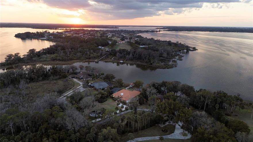 Exquisitely renovated and masterfully reimagined, this direct Lake Dora estate represents a rare acquisition opportunity along the celebrated Harris Chain of Lakes, a turnkey waterfront residence where design excellence and lifestyle prestige converge in harmony. From the moment of arrival, an extraordinary way of life unfolds on the water and on land, where sailboat regattas glide across the horizon, championship fishing awaits offshore, and sunset cruises begin from your private boathouse just near your door. Festivals, boutique shopping and acclaimed dining in historic Mount Dora are equally within effortless reach, creating a seamless blend of leisure, culture and recreation. Privately on an expansive 1.17-acre cul-de-sac home site, the setting ensures a level of exclusivity rarely found along the lakefront. Inside, soaring 12- to14-foot ceilings crown the principal living spaces, unveiling a grand open layout designed for elevated entertaining and everyday comfort alike. Every surface reflects the home’s comprehensive renovation, where curated finishes and jaw-dropping décor create a visual experience as impressive as the surrounding water views. Spanning more than 4,700 square feet of living space, the residence is further enhanced by an oversized three-car garage, an impressively sized pool, and an extraordinary 1,000 square foot terrace overlooking the pool, boathouse and shimmering lake beyond, soon to be elevated further by the addition of a bespoke summer kitchen, designed to transform alfresco dining and sunset gatherings into effortless waterfront entertaining. Life on Lake Dora unfolds at a gentler, more inspired rhythm. Mornings begin with coffee on the dock as mist rises from glassy waters, afternoons invite boating, paddleboarding and cruising the scenic shorelines of the Chain, and evenings conclude beneath painted skies as golden sunsets reflect endlessly across the horizon. Yet the lifestyle extends far beyond the shoreline. Moments away, Mount Dora enriches daily life with its storybook charm and vibrant social energy. Brick-lined streets lead to art galleries, antique markets, wine walks, boat shows, and year-round festivals that animate the town with celebration and sophistication. Waterfront restaurants, boutique cafés, and curated shops create an atmosphere relaxed and refined, a rare pairing that defines this beloved lakefront enclave. For the discerning buyer, a masterfully renovated residence of this scale and presence on Lake Dora is not simply a home but a legacy offering, an opportunity to secure move-in-ready luxury in one of Central Florida’s treasured waterfront corridors, where the Harris Chain lifestyle delivers endless miles of adventure, beauty and timeless lakefront living.