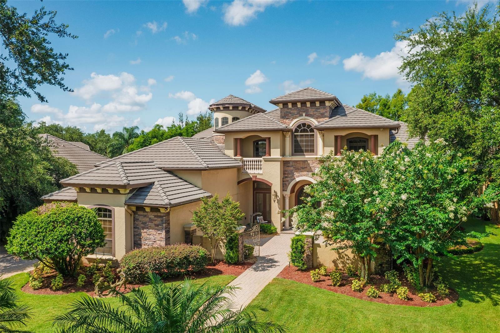 Experience luxury waterfront living in the prestigious gated community of Keene's Pointe. This custom estate offers over 6,000 sq ft of elegant living space with 5 bedroom ensuites and a full pool bath with shower and powder room off of the Theater. A chef's kitchen with stainless-steel appliances, gas range open to the breakfast nook and family room. Perfect for entertaining, the formal dining room features a Butler’s Pantry with wet bar and wine two wine refrigerators. Additional features include an office, bonus room with sauna and expansive second floor loft with full wet bar.
The covered lanai offers motorized screens, summer kitchen and plenty of space for dining and lounging in the shade. The open-air pool features a spa and sunshelf. Rounding out the features of this property is the private boat dock on Lake Burden. Take in sunsets and nightly fireworks as you enjoy all this Florida lakefront has to offer.