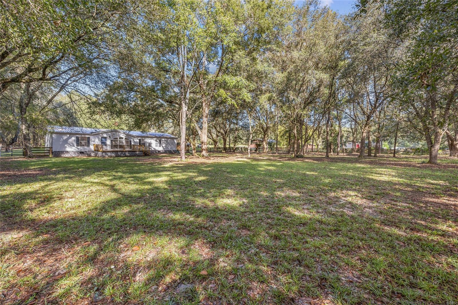Nestled on nearly 10 acres just outside of downtown High Springs, this beautifully wooded property offers a rare combination of privacy, functionality, and convenience. Located on a paved road and surrounded by mature oak trees, this is a peaceful country retreat with all the right upgrades—just a short drive from both Gainesville and Alachua. The 1,620 sq ft home features 3 spacious bedrooms and 2 full bathrooms with a comfortable and practical layout. Inside, you’ll find newer laminate flooring throughout the entire home, giving the space a clean and updated feel. The kitchen is equipped with granite countertops and plenty of cabinet space, flowing easily into the living and dining areas. The home also boasts a newer metal roof and a newer A/C system, making it truly move-in ready. Step outside to enjoy the new front and side decks, perfect for morning coffee or evening sunsets under the oaks. The area surrounding the home has been cleared for ease of use, while the rest of the 9.82-acre parcel remains wooded, providing both shade and seclusion. The property is partially fenced around the house—ideal for pets, gardening, or small livestock. In addition to the home, this property offers exceptional utility with two large barns. The first barn includes two roll-up doors, a concrete floor, and is fully wired with electric—ideal for a workshop, storage, or hobby space. The second barn also features a roll-up door, concrete floor, and electric, plus an attached carport for added functionality. Whether you're into antique cars, woodworking, automotive projects, or need space for farm equipment, these barns are ready for it all. With no HOA and no deed restrictions, you’ll have the freedom to use the land as you please—whether you're dreaming of a homestead, small farm, or simply want room to roam. Just 10 minutes to downtown High Springs, 15 minutes to Alachua, and under 30 minutes to Gainesville, this property offers the best of both worlds: quiet country living with city conveniences close by.