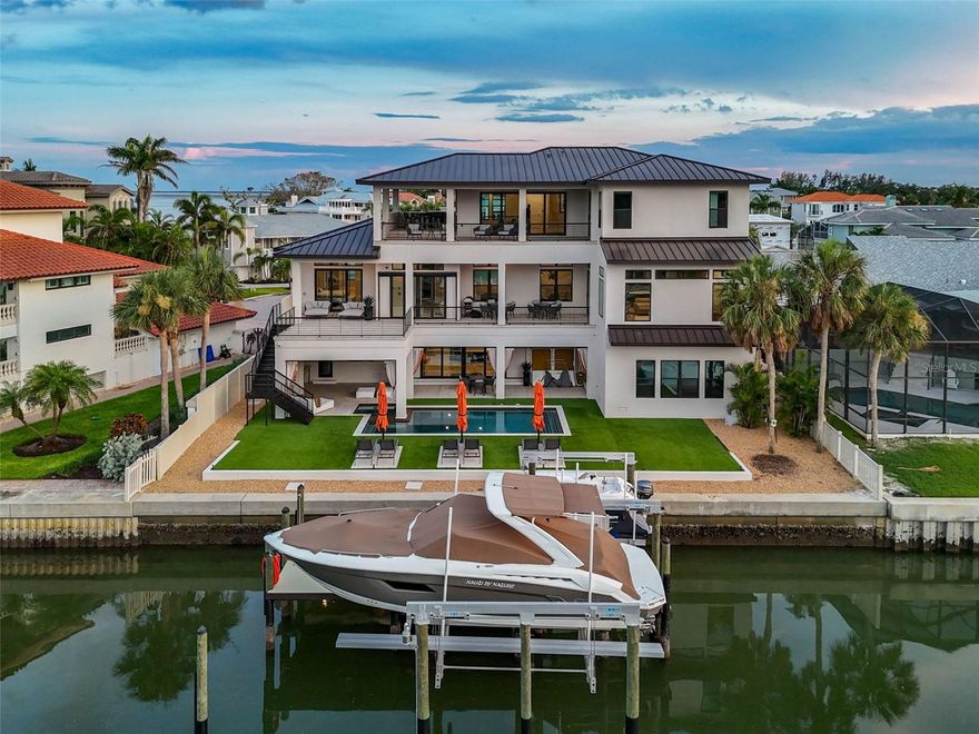 A modern coastal masterpiece, thoughtfully engineered for enduring elegance and the ultimate waterfront lifestyle. Constructed totally custom in 2022, offering 4 bedrooms, 4 full baths, 2 half baths, over 5,500 sq ft of air-conditioned living space, and more than 10,700 sq ft under roof including expansive patios and a 3,500 sq ft air-conditioned garage with a professional quality gym on the ground level. Designed for long-lasting ownership and true peace of mind, the home is constructed with concrete block on the first level, a ZIP wood system for upper floors, over 59 pilings tied to the full footer system, hurricane-impact PGT windows and sliders, spray foam insulation on all exterior walls and roof, plus batt insulation for interior sound reduction. An aged bronze standing seam metal roof, whole-home Generac generator, twin tankless propane water heaters, and a 500-gallon buried propane tank add durability and resilience. Inside, no detail was overlooked — European oak wide-plank floors run throughout, complemented by Porcelanosa tile in all bathrooms and main laundry. Every door features Baldwin solid brass handles. The gourmet kitchen is outfitted with Sub-Zero and Wolf smart appliances, dual 11-ft islands with waterfall edges, custom Busby cabinetry with accent lighting, a separate pantry, and a dedicated coffee bar. All countertops throughout are Cambria quartz with lifetime chip repair. The primary suite is a true retreat with a private office and an additional flex room along with a spa-like bath featuring a huge no-threshold shower with linear drain, freestanding tub, custom vanities, built-ins, and electric privacy screens. The home includes a SONOS wireless sound system, Lutron Caseta smart dimmers, and automated Hunter Douglas window treatments throughout. Outdoor living is resort-inspired with multiple lanais and decks finished in ¾” porcelain tile, a PebbleTec pool with white travertine coping, dual in-pool spas with Pentair automation, Shawgrass artificial turf, triple built-in umbrellas, and a fully equipped dock with a 20,000 lb boat lift, additional lift for smaller watercraft, full-length aluminum walkways, under-dock blue lights, and dedicated power and water at every slip. The oversized garage (up to 10 cars) features a dedicated A/C unit, epoxy floors, custom flake finish, a pro-grade gym with Rogue, REP, and Titan equipment, and a locking storage closet. This is a rare opportunity to own a true architectural gem where every detail from the structural engineering to the finishes was designed to deliver luxury, security, and the ultimate waterfront lifestyle. Make your private appointment today to discover the pinnacle of modern coastal living!