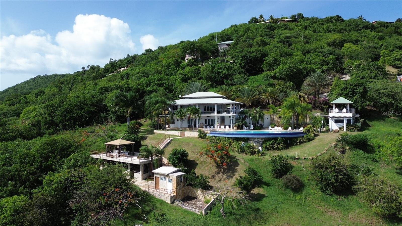 Let yourself be transported upon entry into this grand home located in Culebra, Puerto Rico, known for its crystal-clear waters, swimming areas, and diving sites. This sunny and spacious 5-bedroom, 6.5-bathroom home boasts ocean views from every room, as well as a terrace, balcony, and infinity pool! The stunning property is approximately a 10-minute walk to the beach and is very close to town and restaurants. The new horse stables have never been used and can be converted into a suite with a bathroom and kitchenette. The property is serviced by a septic tank and features AC in all rooms and living areas.
This is a two-level home with two separate gazebos. On the first floor (entrance), you'll find a fully equipped kitchen that seats up to 10, with two 33-bottle wine coolers and a double oven. Each room has its private entrance. The first floor includes 4 bedrooms, including 2 master suites: the first master suite has a king-size bed, TV, private bathroom, and chaise lounge. The second master bedroom has a king-size bed, mini fridge and microwave, private bathroom, and TV. The third bedroom features 2 bunk beds (each with a full-size bed on the bottom and a single bed on top, sleeping 6), TV, and a private bathroom. The fourth bedroom or studio has a queen-size bed, private bathroom, 2 sofas, and is adjacent to the living room with SAT/Dish and DVD player. Additional amenities include laundry facilities, an outdoor shower in the pool area, a lounge chair, large sofa, and a gas barbecue.