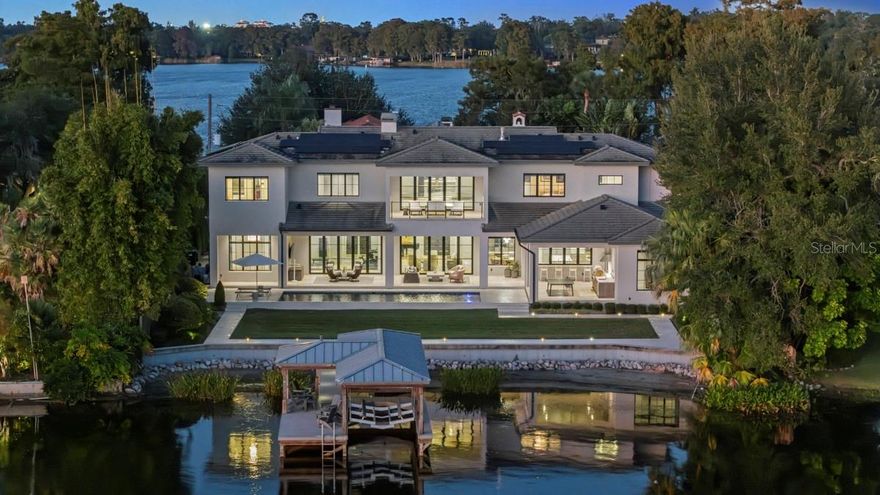 Under contract-accepting backup offers. Spectacular lakefront estate on the eastern shore of Lake Rowena. Positioned between Lake Rowena and Lake Sue in the sought-after Merritt Park/Rose Isle neighborhood, this stunning five-bedroom, five-and-one-half-bath lakefront residence represents the pinnacle of modern design and craftsmanship. Built in 2020, this custom home showcases an extraordinary level of detail throughout, from architectural and construction excellence to thoughtfully curated interior finishes and state-of-the-art technology. The main level is defined by elegant mud-set limestone floors and soaring spaces that flow seamlessly from room to room. The breathtaking great room, framed by a wall of La Cantina folding doors, opens to the sparkling pool and serene lake views beyond. A designer kitchen features a chef’s dream appliance suite including a Wolf 48-inch dual fuel range, 36-inch Sub-Zero refrigerator and freezer, integrated Miele coffee system with direct water connection, warming drawer and an expansive walk-in pantry. La Cantina folding windows connect the kitchen to the outdoor dining and summer kitchen, creating the ultimate indoor/outdoor entertaining experience. Additional first-floor highlights include a lakeside bedroom (converted to an office), a private guest suite with en-suite bath, a glass-enclosed flex room (used as fitness room) and a spacious common room conveniently off the kitchen. Two separate two-car garages, each equipped with Tesla chargers, one with a drop-off zone with access to a well-appointed laundry room featuring ample storage and a dog-wash shower. The staircase and elevator ascend to the second floor, where a stunning glass-railed gallery overlooks the great room below. Another wall of La Cantina folding doors opens to a large covered balcony, an ideal vantage point for taking in elevated lake views. The primary suite is a private retreat with a gas fireplace, a spa-inspired bath with soaking tub and steam shower, and dual walk-in closets. Two additional bedroom suites, each with en-suite baths and walk-in closets, and an additional laundry room complete the upper level. Designed for seamless indoor/outdoor living, the expansive 1,250-square-foot covered lanai features motorized screens, multiple sitting and dining areas, and a fully equipped summer kitchen. The 40-foot heated saltwater pool and lakeside lanai lead to the private covered dock with boat lift, dual jet ski lift, and hot/cold outdoor shower, ideal for lakefront living and entertaining. This advanced Smart Home offers every modern convenience including Lutron lighting and automated window treatments, Starlink, cable, and fiber connectivity, Tesla solar roof panels, and a Tesla Powerwall System for whole-house battery backup and energy efficiency. Just minutes from downtown Winter Park and downtown Orlando, this home offers effortless access to top-rated public and private schools, AdventHealth Rollins Campus, the Orlando Museum of Art, Dr. Phillips Center for the Performing Arts and the Kia Center. Lakefront living at its finest, sophisticated, serene and meticulously designed for today’s discerning lifestyle.