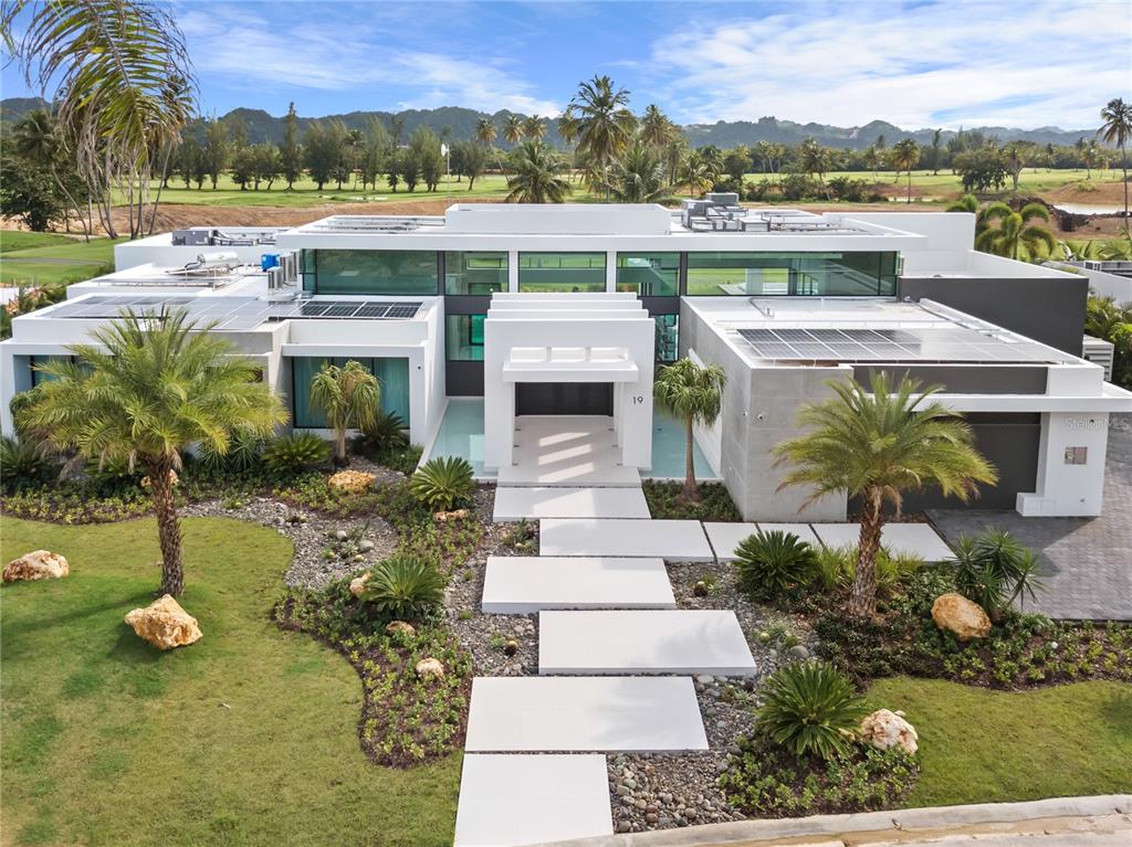 Featured in Architectural Digest Spain and design magazine Modo de Vida, this stunning contemporary home was designed for a lifestyle of leisure. Just steps from the DB Clubhouse, this property has 5 spacious bedrooms, 4 full baths, 2 half baths, and top of the line entertainment facilities, including a heated pool, outdoor bar, wine cellar, and golf simulator.
Premium landscaping features such as dual fountains at the entryway and designer lighting across the yard make this home stand out amongst others in the area. An upgraded driveway leads to a spacious garage with more than enough room for two cars and two golf carts, plus plenty of storage.
The floor plan is designed to maximize views of the nearby golf course and surrounding mountain scenery. With 18” ceilings and floor-to-ceiling windows, the home is filled with natural light.
This home boasts the finest European finishes throughout. Spanish porcelain tile flooring gives a beautiful marble effect with improved durability, and in the kitchen, custom Italian cabinets create a modern minimalist aesthetic, whilst an oversized island with two waterfalls adds a sense of grandeur.
Wine enthusiasts will appreciate the temperature- and humidity-controlled cellar, whilst the Trackman Simulator will appeal to keen golfers. At the rear of the property, this home has a large, heated swimming pool with a sun shelf and spa pool, a gas fire pit, and a full-sized outdoor bar with an 85” TV and luxury grill.
No expense has been spared to future-proof this home, with custom-programmed Vitrea light switches, top of the range sound system, and ACMaster installed throughout the home. 100 40kw solar panels have been installed on the roof, with a 13.5kwh Tesla Powerwall and backup generator to provide almost a week’s worth of power.