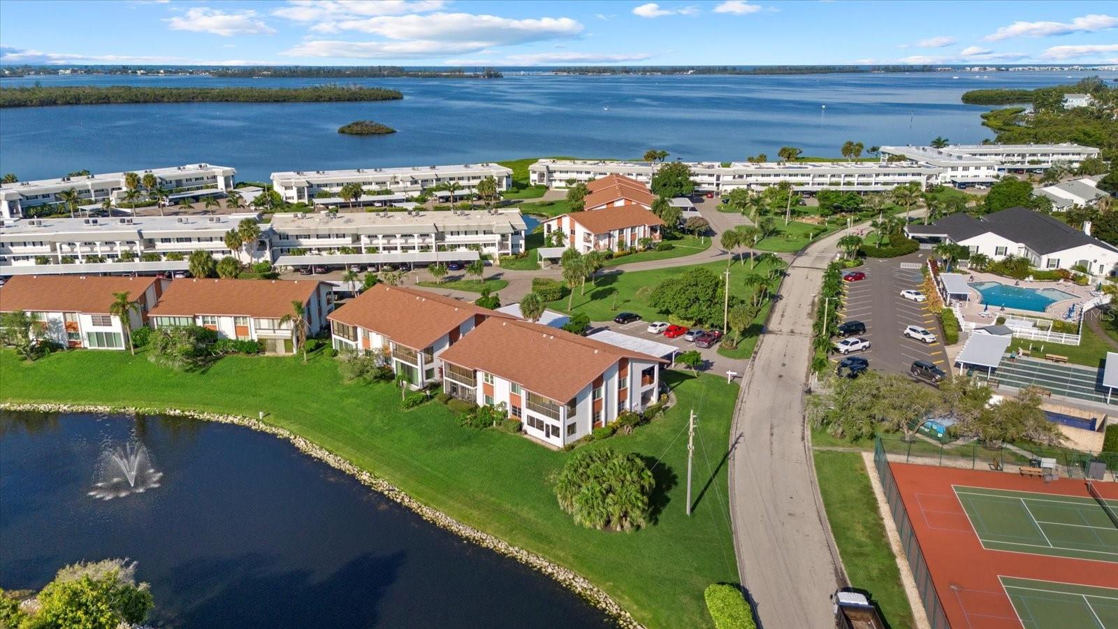 Lock-and-leave coastal living just a 5 minute drive or 3 mile bike ride from Anna Maria Island! Welcome to Mount Vernon, a beautifully maintained 55+ community along Sarasota Bay. This is the best priced first floor unit available with the added benefit of being an unit and covered parking. The location couldn't be any better, just across the street from the community amenities with a water view. Amenities include a clubhouse, heated pool, tennis, pickleball, putting green, shuffleboard, scenic walking paths, kayak launch, and boat docks. Step inside to a open layout with an all weather sunroom, perfect for catching sunrises over the water. The spacious layout offers comfortable living with an open concept design. The primary bedroom is equipped with dual closets plus an ensuite bathroom with dual sinks and a walk-in shower with grab bars. The secondary bedroom has ample storage with a walk-in closet. The monthly fee includes water, sewer, trash, pest control, cable, internet, exterior maintenance, landscape maintenance, and building insurance- so your essentials are bundled into one predictable payment. This West Bradenton location puts beaches, dining, and healthcare all within a short drive. Florida living, made easy!