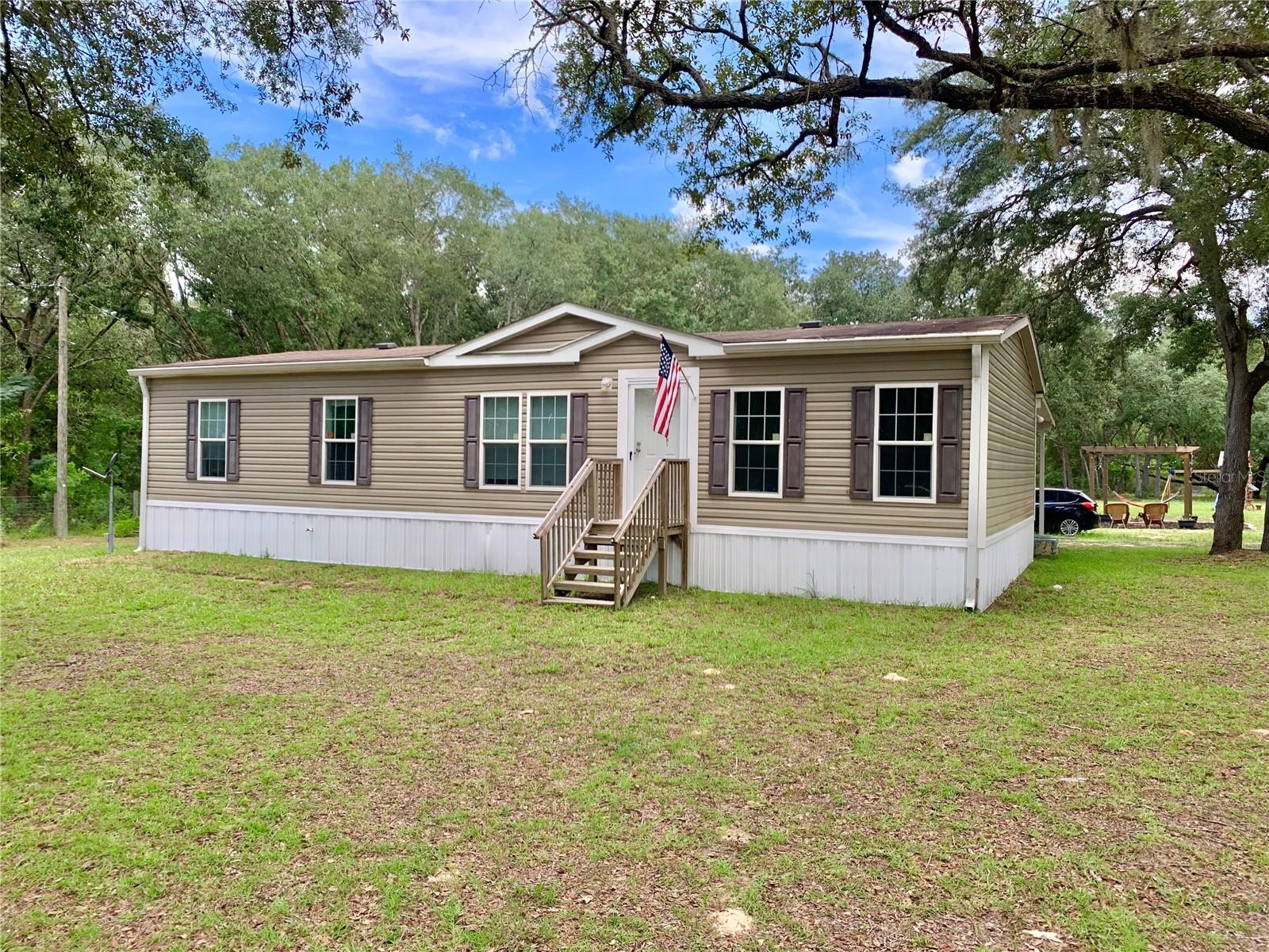 Beautiful 3/2 manufactured home on 1.58 acres of fenced property. This home features a wonderful open floor plan perfect for entertaining. The kitchen is spacious with lots of counter space, granite countered island, stainless steel farmhouse sink, glass tile backsplash and luxury vinyl tile floors. The dinning area features a decorative tray ceiling with crown molding accents, double French doors lead from the dinning area to the back covered porch. The living room is open to the kitchen and dinning rooms. There is plenty of natural light from the living room windows. The primary bedroom is spacious and offers a large walk in closet. The primary bathroom has a double vanity with storage shelving in-between. There is also additional built in shelving for towel by the walk in shower. The two guest rooms are both spacious with nice closet space and complete with crown molding. The laundry room has extra cabinet space as well as a folding counter and room for a standing freezer. The large back porch is perfect for the mornings or quiet evening to relax under the insulated roofing and ceiling fan. There is a one car carport on the back of the home. A mulched pathway leads to the firepit and pergola area for hammocks or hanging swings. A small storage shed with convey with the property. The property once again is fenced so it is ready for your pets and critters. This is a beautiful home with a great floorplan and lots of nice upgrades. Survey and clean engineering reports are on hand. Schedule a tour today for your next home.