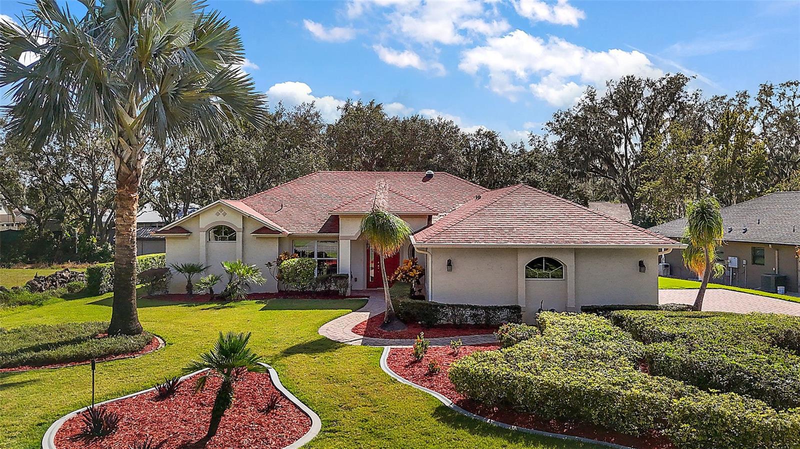 CANAL FRONTAGE TO LAKE EUSTIS, BEAUTIFUL MOVE-IN READY 3 BR HOME IN DESIRABLE VISTA DEL LARGO COMMUNITY. Welcome home to this tranquil, well-established, non-HOA community nestled on the shore of stunning Lake Eustis. Mature oaks and gracefully swaying palm trees greet you as you drive through the community to arrive at this attractive, well-maintained waterfront home just waiting for its new owner. The lush front lawn has concrete curbing for planter beds containing mature shrubs, palm trees, and ponytail palms. Pull into the spacious brick paver driveway, which leads to the side-entry 2-car garage. A paver path beckons you to the covered front door portico and inside to find a light and airy interior brimming with a casual, comfortable elegance. Glorious natural light streams in through large windows to enhance the beauty of the thoughtfully designed interior with high vaulted ceilings, luxury vinyl floors, a serene, neutral color palette, and a spectacular foyer/entry view of the back yard with the sparkling canal to Lake Eustis. Hosting family and friend gatherings and holiday celebrations will be a delight here with a well-designed floor plan. The open living, dining, and kitchen areas flow together seamlessly and offer backyard canal views from the expansive glass sliding pocket door leading to the rear lanai, a vantage point for relaxing in nature with your morning coffee or dining al fresco at sunset. Enjoy flexing your culinary skills in this attractive, well-appointed kitchen with beautiful dark granite counters, custom 42-inch wood cabinetry, and wonderfully efficient storage drawers. All the lovely conveniences and special touches are here, including stainless steel appliances, an ideal walk-in pantry, a Solatube skylight, and a spacious breakfast bar, in addition to the dining area with a panoramic bay window. The handy inside laundry room is adjacent to the kitchen, offering storage cabinetry and a door to the garage. The split bedroom floor plan affords ample privacy for all. The inviting primary suite has high ceilings, a large window providing canal views, and two walk-in closets for all your storage needs. The private en-suite features custom wood cabinetry and dark granite counters, matching the kitchen for a nice continuity. Dual sinks and a spacious counter are coveted features, as is the to-die-for walk-in shower with five showerheads! Two carpeted guest bedrooms share the full hallway bathroom with a tub/shower. As beautiful and cozy as the interior is, you will want to spend abundant time outdoors in the lovely backyard. Drink in gentle breezes coming off the canal waters as you relax on the screened enclosed lanai, or meander down the paver walkway to the water's edge to cast a fishing line. Launch a paddleboard or kayak, or build a boat dock for quick and easy canal access to the open waters of coveted Lake Eustis and the Harris Chain of Lakes. Visit popular waterfront restaurants by boat or spend the day fishing in an area known for plentiful Bass, Crappie, and Bluegill. Whether by car or boat, every fun activity and desired amenity is effortlessly nearby, making this exceptional waterfront property an ideal place to call home.