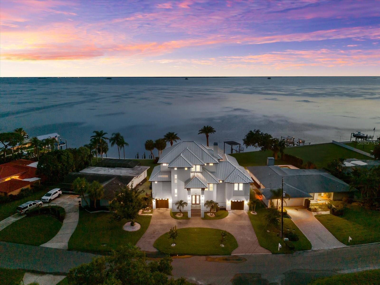 A rare offering where modern elegance meets coastal serenity—welcome to 110 Carlyle Drive, a breathtaking Gulf-front estate nestled on the exclusive shores of Indian Bluff Island. Custom-built in 2022 and meticulously designed for elevated living, this residence commands 80 feet of pristine waterfront along the Intracoastal, with direct access to the Gulf of Mexico.
Beyond the private circular drive, a statement double-door entry sets the tone for the refined interiors that follow. Soaring ceilings, expansive walls of glass, and hand-selected finishes create a luminous, open atmosphere that celebrates the water views from nearly every room. At the heart of the home, a grand great room with a gas fireplace seamlessly flows into the designer chef’s kitchen—complete with solid wood cabinetry, a suite of luxury appliances, and panoramic views that make everyday living feel extraordinary.
The primary suite is a sanctuary of sophistication, framed by water vistas and complete with an indulgent spa bath, dual vanities, and a custom walk-in closet. Upstairs, three additional bedrooms feature en-suite baths and walk-in closets, each designed with space, privacy, and style in mind.
Step outside into your own waterfront resort. A saltwater pool glistens beneath the sun, surrounded by tropical landscaping and expansive outdoor living space, perfect for year-round entertaining. A private dock with a 10,000 lb lift, composite decking, water/electric hookup, and a concrete seawall elevates the boating lifestyle.
Crafted with block construction, a tile roof, impact-rated windows, and timeless architectural elements, this home is equal parts beauty and resilience. Additional features include an oversized four-car garage, golf cart parking, elevator access, and interior laundry.
Located in a quiet, established enclave just minutes from top-rated beaches, golf and country clubs, and downtown Palm Harbor. Zoned for the highly sought-after Palm Harbor University High School.
This is more than a home—it’s a coastal legacy built to last, where every sunrise and sunset is yours to own.