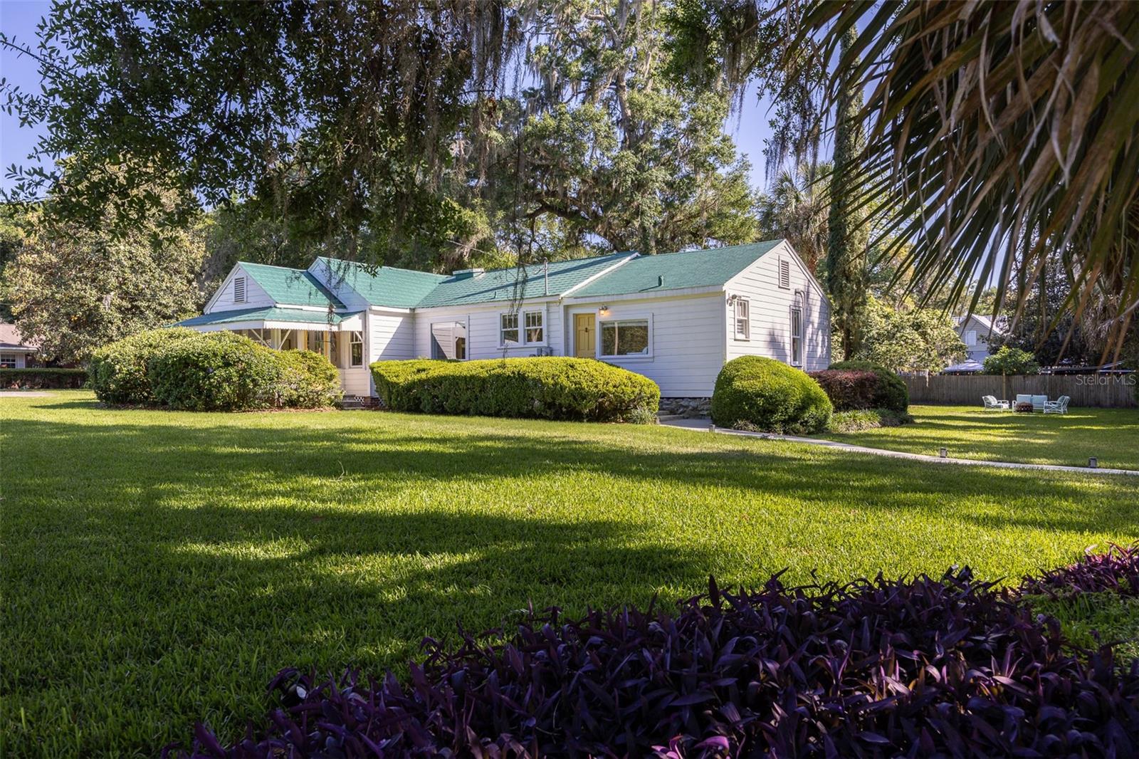 Welcome to your dream retreat in the heart of Historic High Springs! This beautifully renovated 3-bedroom, 2-bath Craftsman bungalow sits on a lushly landscaped ½-acre corner lot on a peaceful side street, just a short walk to the Great Outdoors Restaurant, downtown shops, cafes, bars, and live music and is located just minutes from Blue Springs, Poe Springs, and only a 12-minute drive to Ginnie Springs, thus offering quick access to some of Florida’s most beautiful natural springs. The University of Florida and downtown Gainesville are only 22 minutes away, making this an excellent location for both personal use and investment. Offering the perfect mix of vintage charm and modern upgrades, this home features original wood floors and windows, a fully updated kitchen with Corian countertops, soft-close cabinetry, new appliances (including a dishwasher and dryer), and fully updated plumbing and electrical systems. The spacious layout includes a king-size primary bedroom and two guest bedrooms with queen beds, two full bathrooms and a bright dining area adjacent to the kitchen.
Smart home features include keyless entry, a smart thermostat, security cameras, and a smart TV (included). French doors lead to a stunning covered front porch with vaulted wood ceilings, a hammock swing chair, and a relaxing view of the beautifully landscaped yard. Outdoors, enjoy your own private oasis with a fire pit, grill area, fairy lights, a two-person hammock, and mature trees. The entire yard is fully irrigated and fed by a private spring-fed well, providing fresh drinking water and eliminating water bills. The home is equipped with a UV antiviral air conditioning system for added comfort.
Also included is a detached outbuilding with metal roof, ideal for use as a studio, home gym, or office.
This home has operated successfully as a short-term rental and offers outstanding potential as a vacation home, full-time residence, or turnkey rental property. Comfort bedding, hotel-grade linens, premium bath products, and select antique furnishings can be included, making this a truly move-in-ready opportunity. This one-of-a-kind home won’t last—schedule your private showing today!