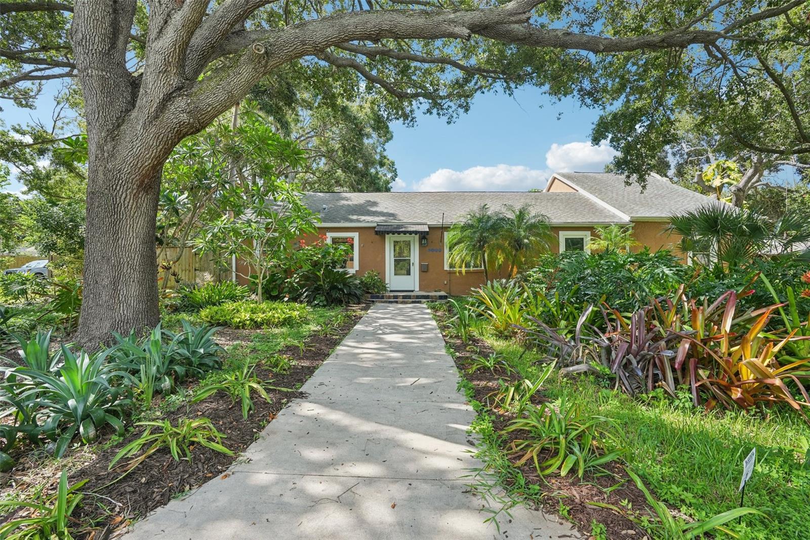 Welcome to this exceptional residence in the heart of St. Petersburg’s highly desirable Historic Kenwood neighborhood—a community known for its tree-lined streets, colorful bungalows, and vibrant arts scene. This property perfectly blends timeless mid-century architecture with tasteful modern upgrades. Built in 1949, the home has been thoughtfully maintained to honor its original character while providing the conveniences expected in today’s market. With over 2,500 square feet of living space on a rare double lot, it delivers both substance and style. From the moment you arrive, the charming façade, lush landscaping, and welcoming front entry set the tone for what awaits inside.
Step through the front door into an interior that feels warm and inviting. The layout flows easily from room to room, creating a space ideal for both everyday living and entertaining. At the heart of the home is the gourmet kitchen, featuring granite countertops, a sleek cooktop, convection microwave, dual sinks, and abundant cabinetry. Its generous prep space and open connection to the living areas make it perfect for casual meals or dinner parties. Adjacent to the kitchen, the spacious grand room offers bamboo hardwood floors, abundant natural light, and views of the lush landscaping and pool. This is the ideal setting for relaxing evenings or lively gatherings. The large primary bedroom is a true retreat, filled with natural light from multiple windows and offering plenty of room for a king-sized bed, sitting area, and more. A generous walk-in closet adds style and function, keeping everything organized and accessible. Additional bedrooms provide comfortable accommodations for guests or flexible space for an office, gym, or hobbies. Outside, the expansive backyard is a private oasis. A custom saltwater pool with a gentle ramp entrance invites you to cool off or simply float in the sun, surrounded by tropical gardens, mature trees, and a greenhouse for year-round gardening. The double lot offers rare extra space for outdoor living—whether sunbathing, dining under the shade, or hosting a barbecue. For hobbyists, the detached garage doubles as a workshop with ample space for tools, projects, and recreational gear. The thoughtful property design allows for generous parking without sacrificing green space. All of this is just minutes from downtown St. Petersburg’s dining, shopping, galleries, waterfront parks, and entertainment. Sports fans will appreciate the proximity to Tropicana Field, and beach lovers can reach the Gulf in no time. Located in FEMA’s non-flood Zone X, this home combines style, practicality, and a prime location into one outstanding offering.