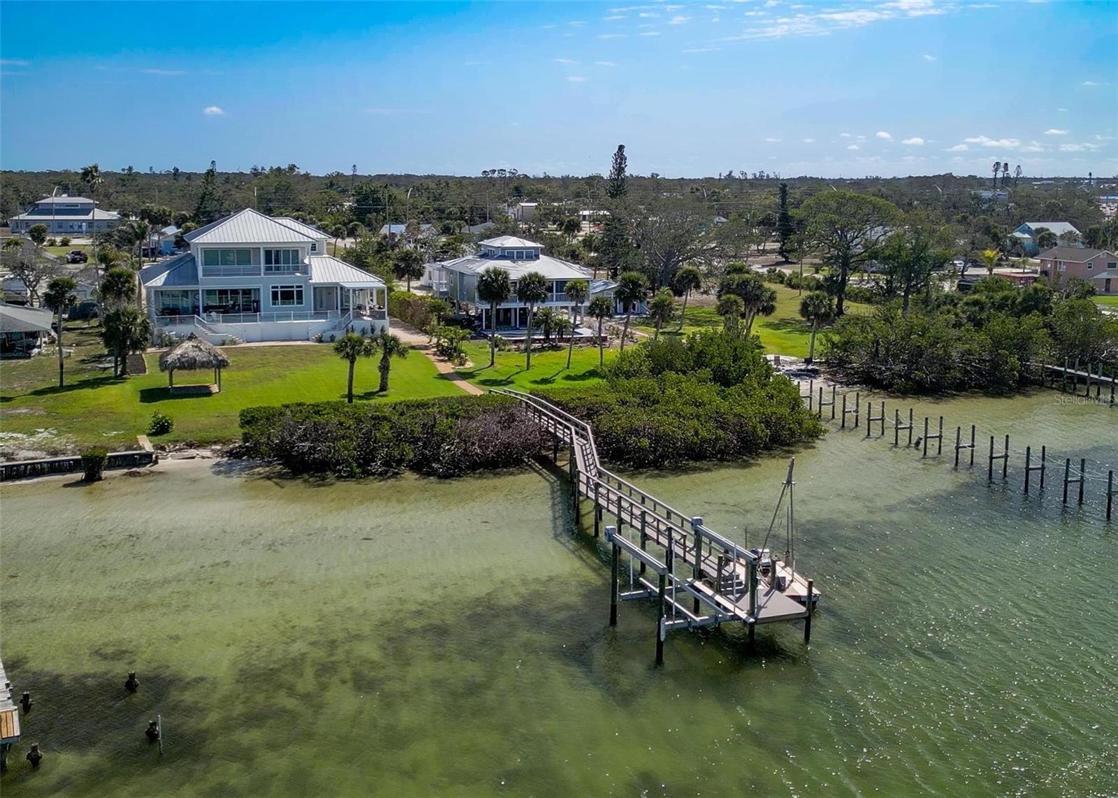 Nestled along the serene shores of Lemon Bay, this stunning two-story residence offers unparalleled access to the Gulf and breathtaking westward views, perfect for enjoying vibrant sunsets. Sitting on a sprawling 1-acre lot, this architectural gem boasts a durable metal roof and soaring high ceilings that enhance its spacious, open-concept design. Comes Fully Furnished. Ceramic tile flows seamlessly throughout the home, complemented by top-of-the-line Thermidor appliances in the gourmet kitchen. Every room, including all bedrooms, showcases expansive views of the bay, ensuring a constant connection to the tranquil waterfront setting.
The master suite is a true retreat, featuring his-and-hers walk-in closets and a luxurious garden tub in the spa-like bathroom. Upstairs, an en-suite bedroom opens to a private balcony, ideal for morning coffee or evening relaxation. The home’s outdoor living spaces are equally impressive, with a travertine-tiled pool deck, a large heated pool, and hot tub for year-round enjoyment. An electric pergola provides shade over the outdoor kitchen, complete with ample space for entertaining. A 170-foot dock extends into the bay, equipped with a boat lift capable of supporting up to 16,000 pounds—perfect for boating enthusiasts. With a grandfathered in Tiki Hut, the property even offers a private beach at low tide, adding a rare and coveted touch of exclusivity.
Convenience meets luxury with the ability to reach nearby restaurants and shopping by boat. In less than a few miles you can be on Manasota key which offers several restaurants and entertainment on Englewood Beach, Middle beach and Manasota Key beach, offering endless coastal adventures. The garage is thoughtfully designed with concrete walls, elevated steps, and an air conditioning unit raised 5 feet to mitigate flood risk, ensuring peace of mind. A 30-amp breaker on the exterior provides RV hookup capability, adding versatility for guests or travel enthusiasts. Just a mile up the road, a lively farmers market draws visitors from near and far, offering a delightful community experience.
With its breathtaking views, modern amenities, and prime waterfront location, this Lemon Bay masterpiece is a rare find—a perfect blend of elegance, functionality, and coastal charm. There was no damage done to the house. The only two things that needed to be replaced / Fixed was the Pool Equipment which is now new and they remodeled the dock.