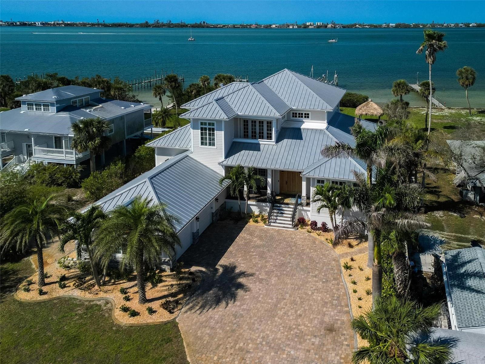Nestled along the serene shores of Lemon Bay, this stunning two-story residence offers unparalleled access to the Gulf and breathtaking westward views, perfect for enjoying vibrant sunsets. Sitting on a sprawling 1-acre lot, this architectural gem boasts a durable metal roof and soaring high ceilings that enhance its spacious, open-concept design. Comes Fully Furnished. Ceramic tile flows seamlessly throughout the home, complemented by top-of-the-line Thermidor appliances in the gourmet kitchen. Every room, including all bedrooms, showcases expansive views of the bay, ensuring a constant connection to the tranquil waterfront setting.
The master suite is a true retreat, featuring his-and-hers walk-in closets and a luxurious garden tub in the spa-like bathroom. Upstairs, an en-suite bedroom opens to a private balcony, ideal for morning coffee or evening relaxation. The home’s outdoor living spaces are equally impressive, with a travertine-tiled pool deck, a large heated pool, and hot tub for year-round enjoyment. An electric pergola provides shade over the outdoor kitchen, complete with ample space for entertaining. A 170-foot dock extends into the bay, equipped with a boat lift capable of supporting up to 16,000 pounds—perfect for boating enthusiasts. With a grandfathered in Tiki Hut, the property even offers a private beach at low tide, adding a rare and coveted touch of exclusivity.
Convenience meets luxury with the ability to reach nearby restaurants and shopping by boat. In less than a few miles you can be on Manasota key which offers several restaurants and entertainment on Englewood Beach, Middle beach and Manasota Key beach, offering endless coastal adventures. The garage is thoughtfully designed with concrete walls, elevated steps, and an air conditioning unit raised 5 feet to mitigate flood risk, ensuring peace of mind. A 30-amp breaker on the exterior provides RV hookup capability, adding versatility for guests or travel enthusiasts. Just a mile up the road, a lively farmers market draws visitors from near and far, offering a delightful community experience.
With its breathtaking views, modern amenities, and prime waterfront location, this Lemon Bay masterpiece is a rare find—a perfect blend of elegance, functionality, and coastal charm. There was no damage done to the house. The only two things that needed to be replaced / Fixed was the Pool Equipment which is now new and they remodeled the dock.