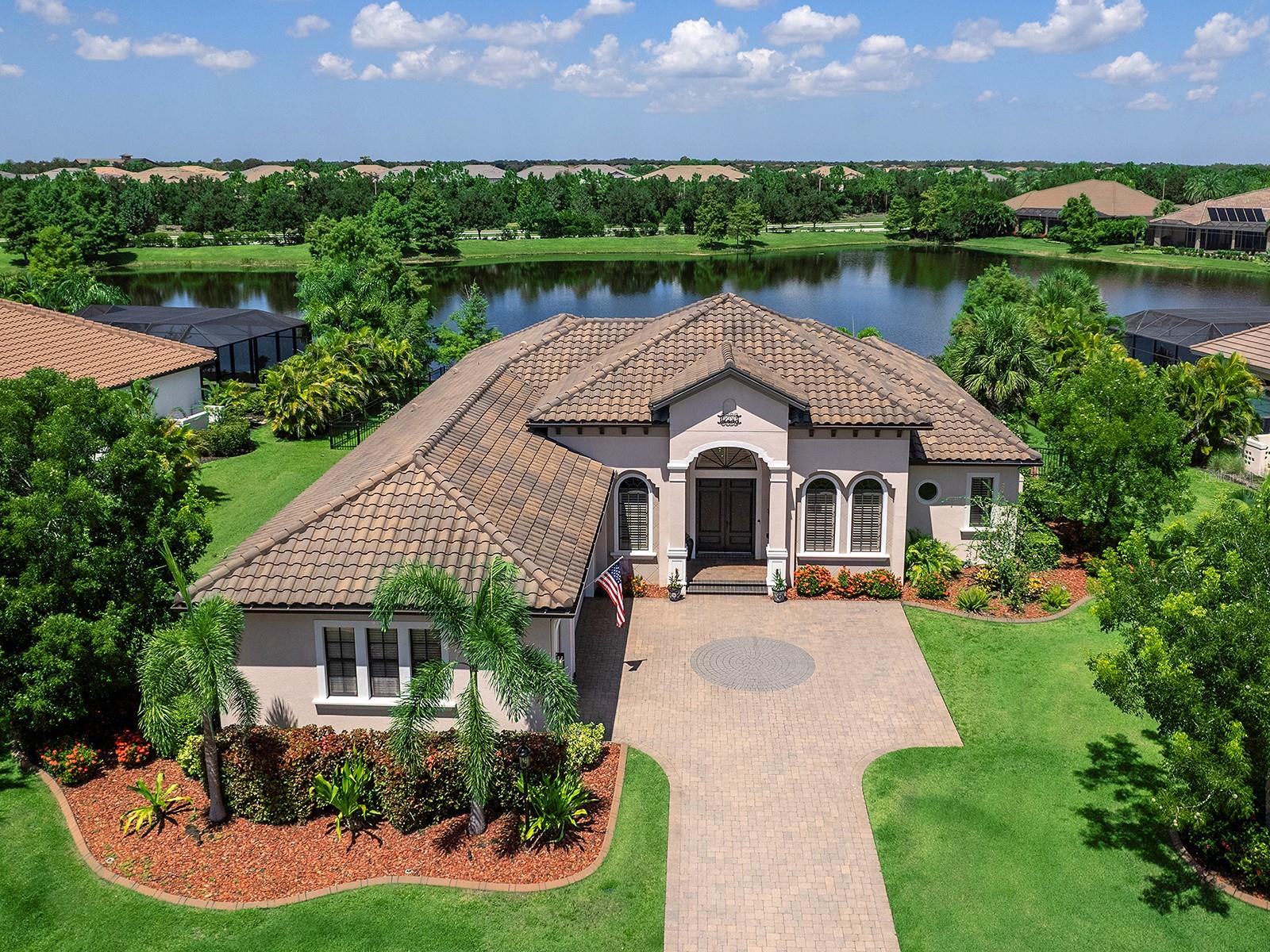 Sunset Views Over the Lake in Country Club East! This custom John Cannon home sits on one of the largest homesites in Seacroft, a premier enclave of Country Club East. Designed with 4 bedrooms, 3.5 baths, and a private office, the residence takes full advantage of its setting with sweeping lake vistas, unforgettable sunset views, and an expansive fenced yard. The great room features wood floors, 12’ ceilings, new designer lighting and ceiling fans, and 10’ impact sliders with interior remote-controlled shades for effortless comfort. The gourmet kitchen showcases a 48” Sub-Zero refrigerator, new Bosch dishwasher, oversized island, walk-in pantry with custom shelving, wood cabinetry, and beam-and-beadboard ceiling detail, all opening to a spacious dining area and lanai beyond. The owner’s suite combines comfort and style with wood flooring (2023), serene lake views, dual custom walk-in closets, granite vanities, an oversized shower with rainhead and dual faucets, and a soaking tub. Three additional bedrooms—one with en-suite—plus a powder room with updates (2024) complete the thoughtful plan.
Outdoor living shines with an oversized spa, outdoor kitchen with Lynx grill, refrigerator, and granite bar, new no-see-um screens (2023), hurricane-rated drop-down screens added in 2024, overhead cage and landscape lighting, and a retractable screen at the double front doors for fresh cross-breezes. The oversized lot and large fenced yard (2023) provide privacy and plenty of space rarely found in this community.
Recent updates and upgrades include: freshly painted interior/exterior (2023), impact windows and doors, a whole-house generator (2023), 3-zone HVAC with allergen-friendly blue light, plantation shutters and wood blinds (2024), new washer & dryer (2025), luxury vinyl plank flooring in bedrooms 2–4 (2023), and all mounted TVs (2023) throughout the home included—two on the lanai, plus the great room, primary suite, and bedrooms. The garage is climate-controlled with a mini-split A/C (2023), Icynene insulation, custom flooring, overhead storage, and built-in cabinetry. Country Club East offers three resort-style pools, fitness, and optional membership at Lakewood Ranch Golf & Country Club. Just outside the gates, enjoy Lakewood Ranch’s vibrant lifestyle with Waterside Place, Main Street, world-class dining, shopping, medical facilities, and Gulf beaches all minutes away.